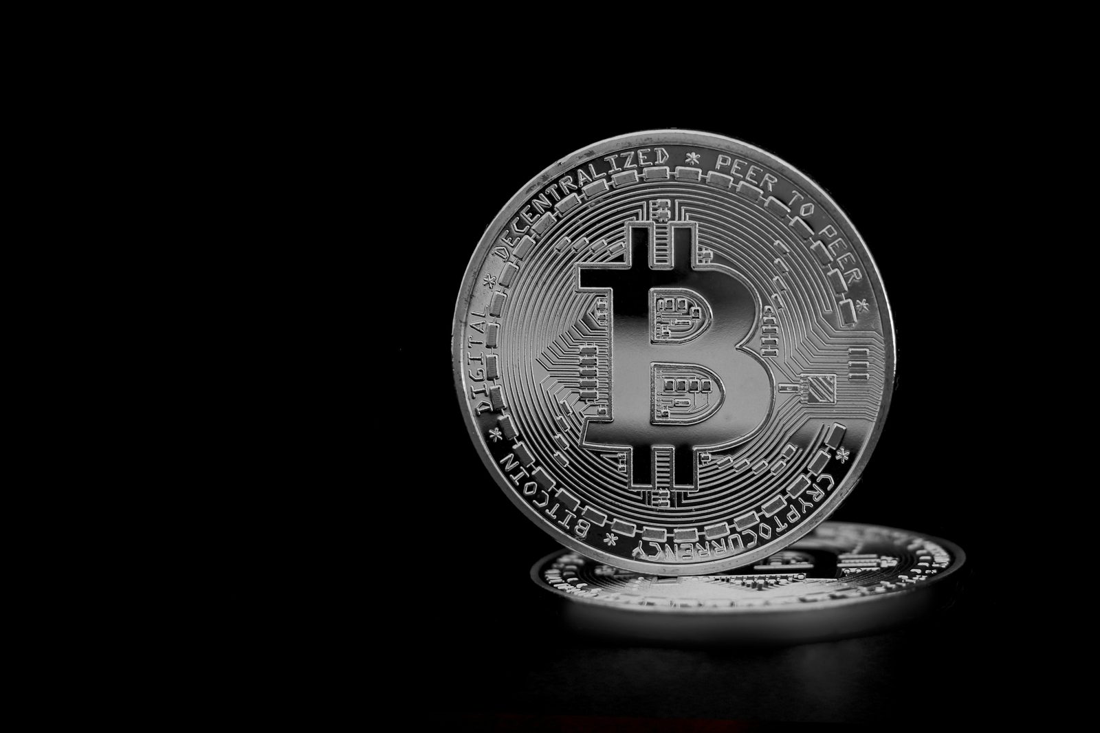 Moneda plateada de Bitcoin en primer plano con el texto BITCOIN DIGITAL PEER TO PEER sobre fondo negro.