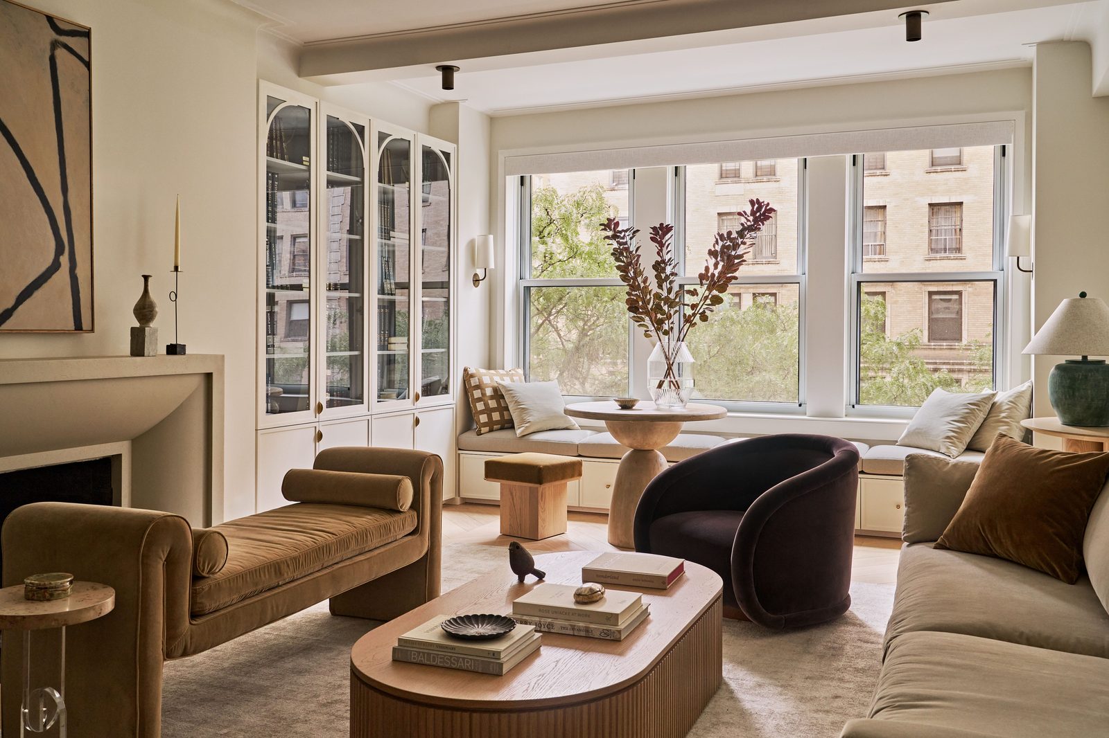 Sala de estar moderna con sofá color tostado, sillón oscuro y mesa de centro ovalada junto a una ventana grande