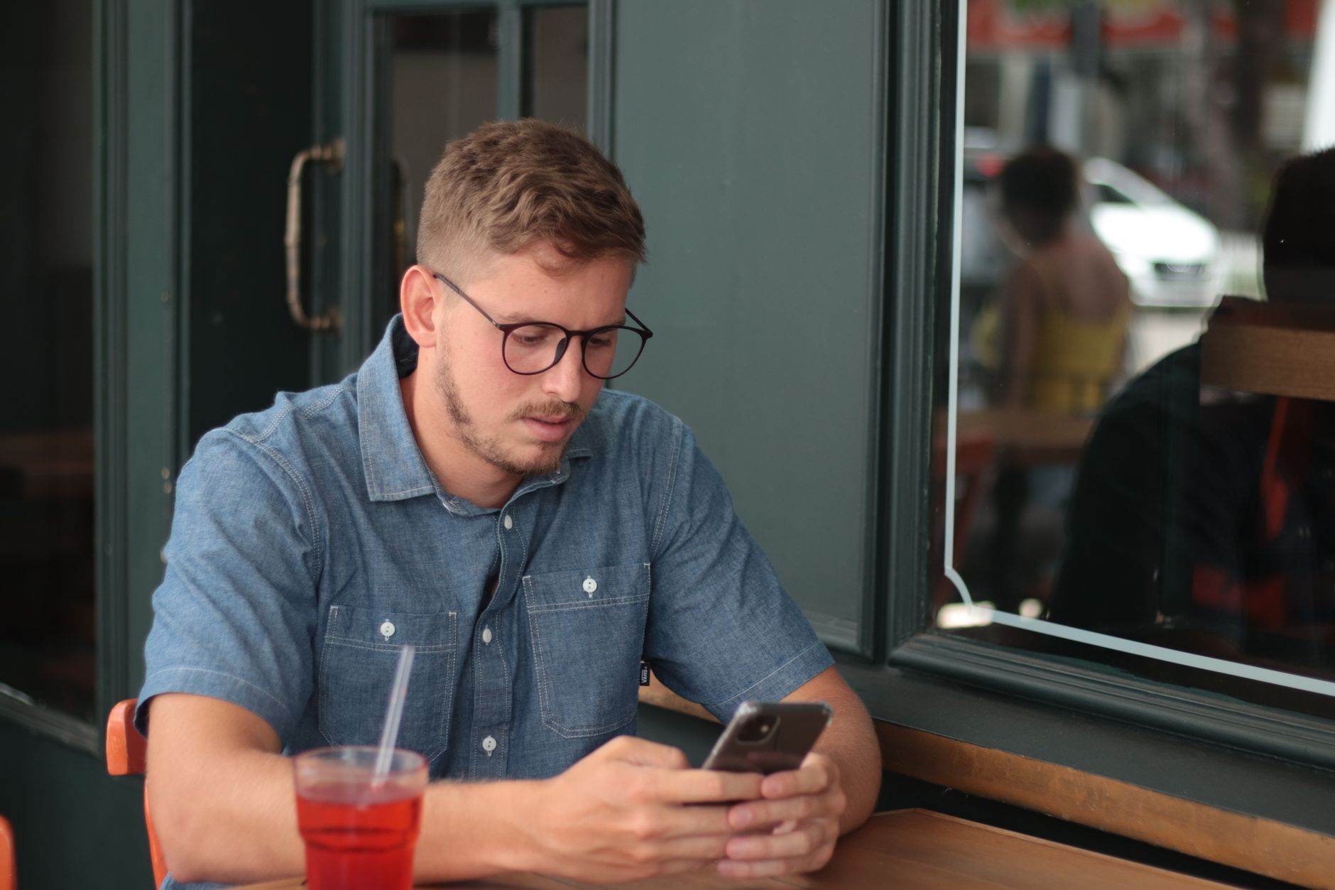 Un joven revisa su teléfono sentado junto al ventanal de una cafetería