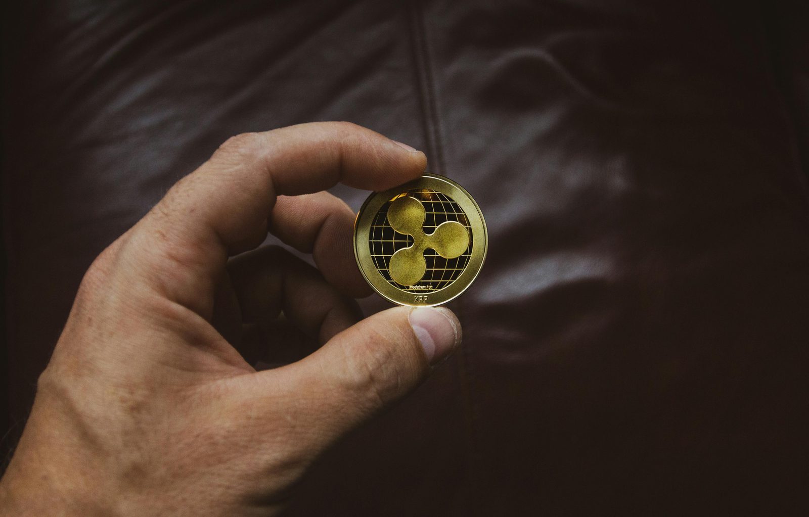 Mano sosteniendo una moneda dorada con el símbolo de Ripple sobre un fondo oscuro y texturizado