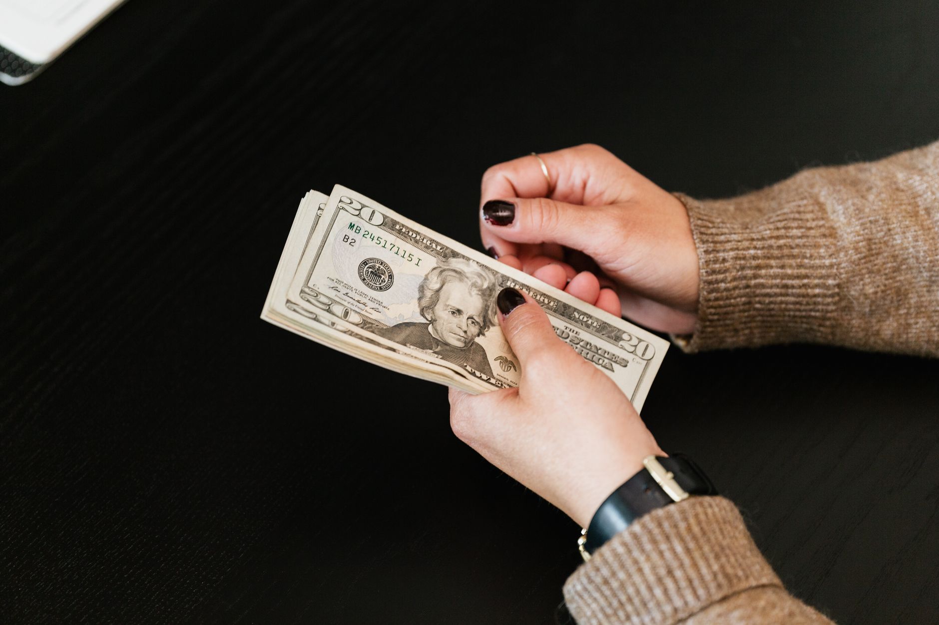Manos contando billetes de veinte dólares sobre una mesa oscura