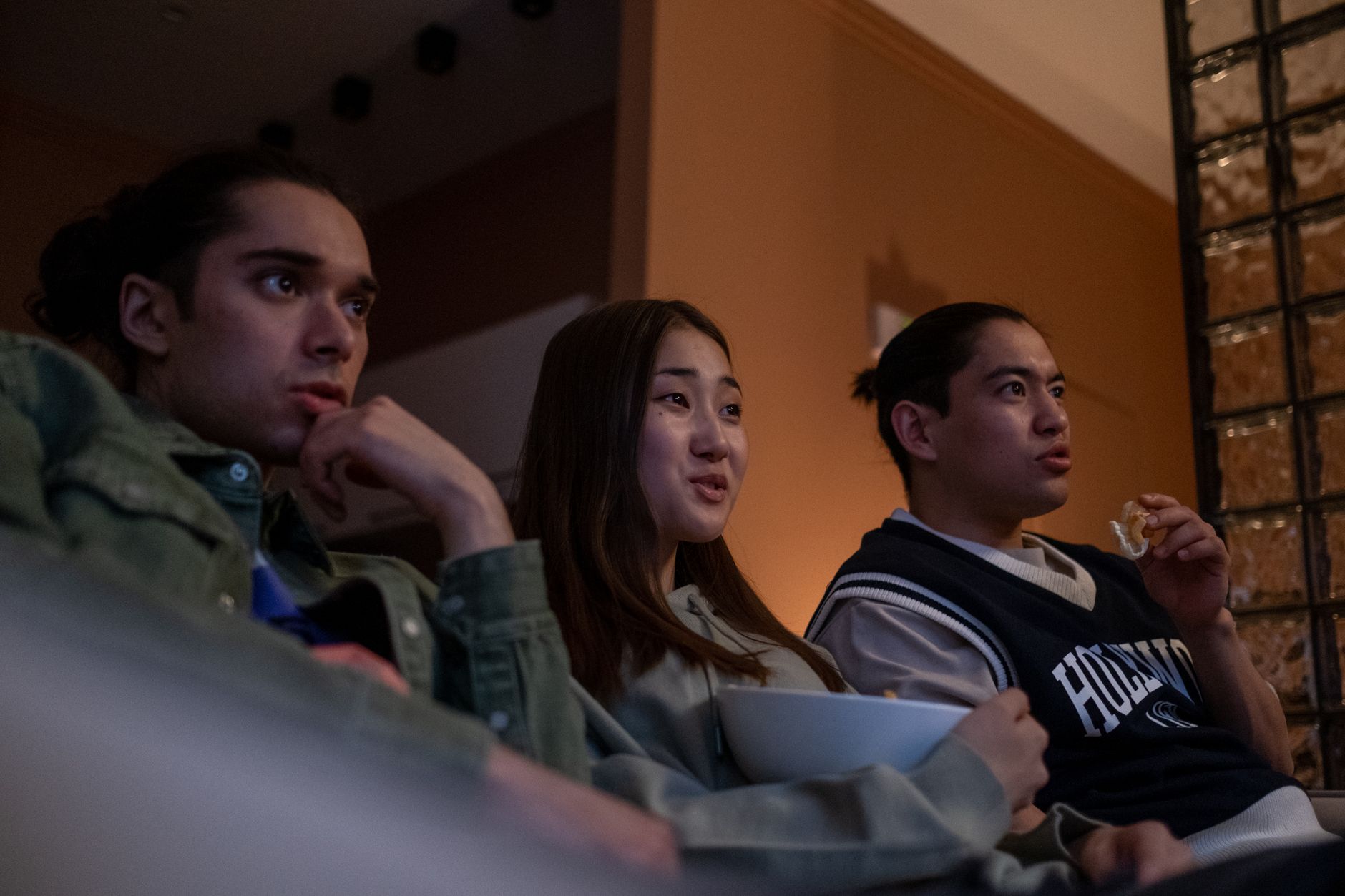 Tres jóvenes ven juntos una serie en el sofá compartiendo un bol de palomitas