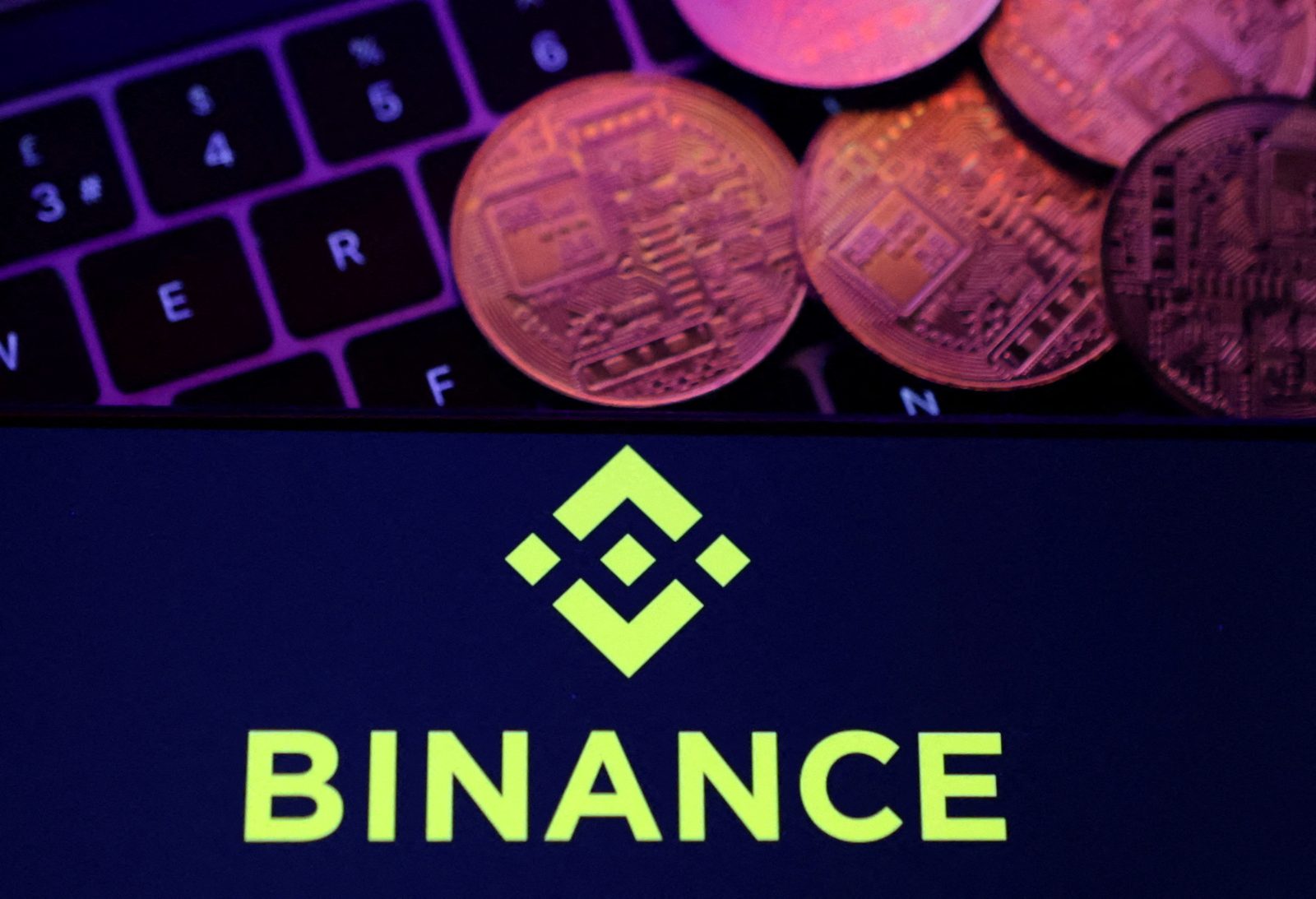 Monedas de criptomoneda doradas sobre un teclado oscuro, con el logo y nombre de Binance en una pantalla debajo