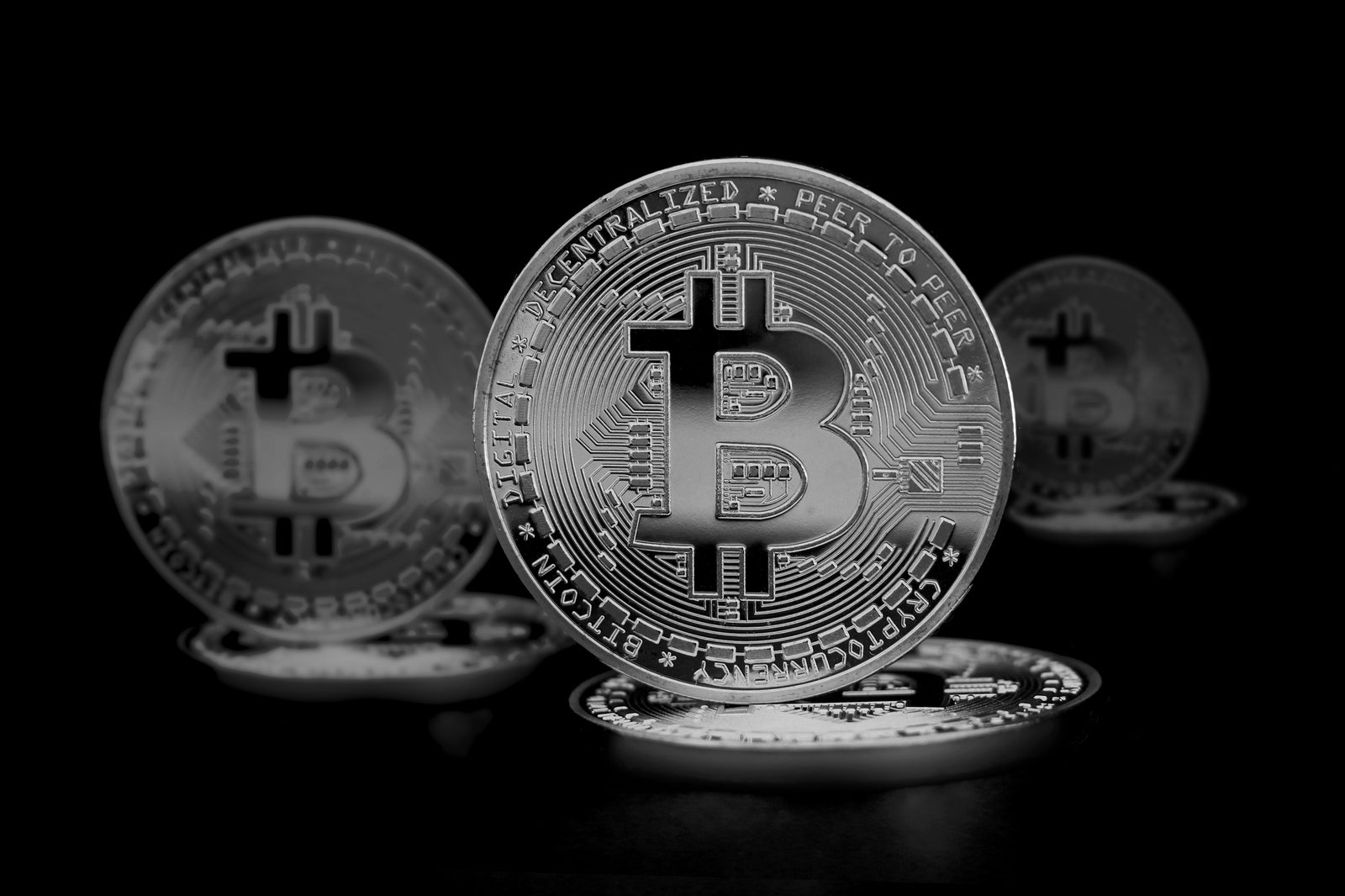 Monedas plateadas de Bitcoin en blanco y negro con una en primer plano y otras desenfocadas al fondo