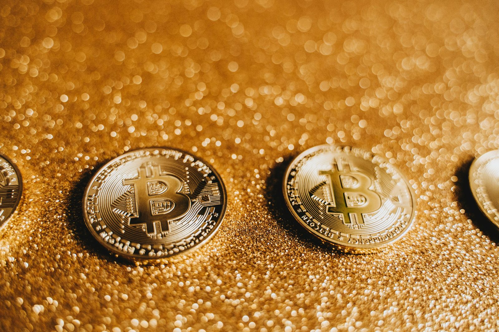 Monedas doradas con el símbolo de Bitcoin descansan sobre una superficie brillante con purpurina.