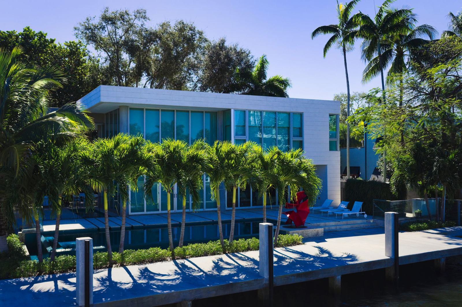Casa moderna de lujo con fachada de vidrio, piscina y palmeras en un barrio residencial exclusivo