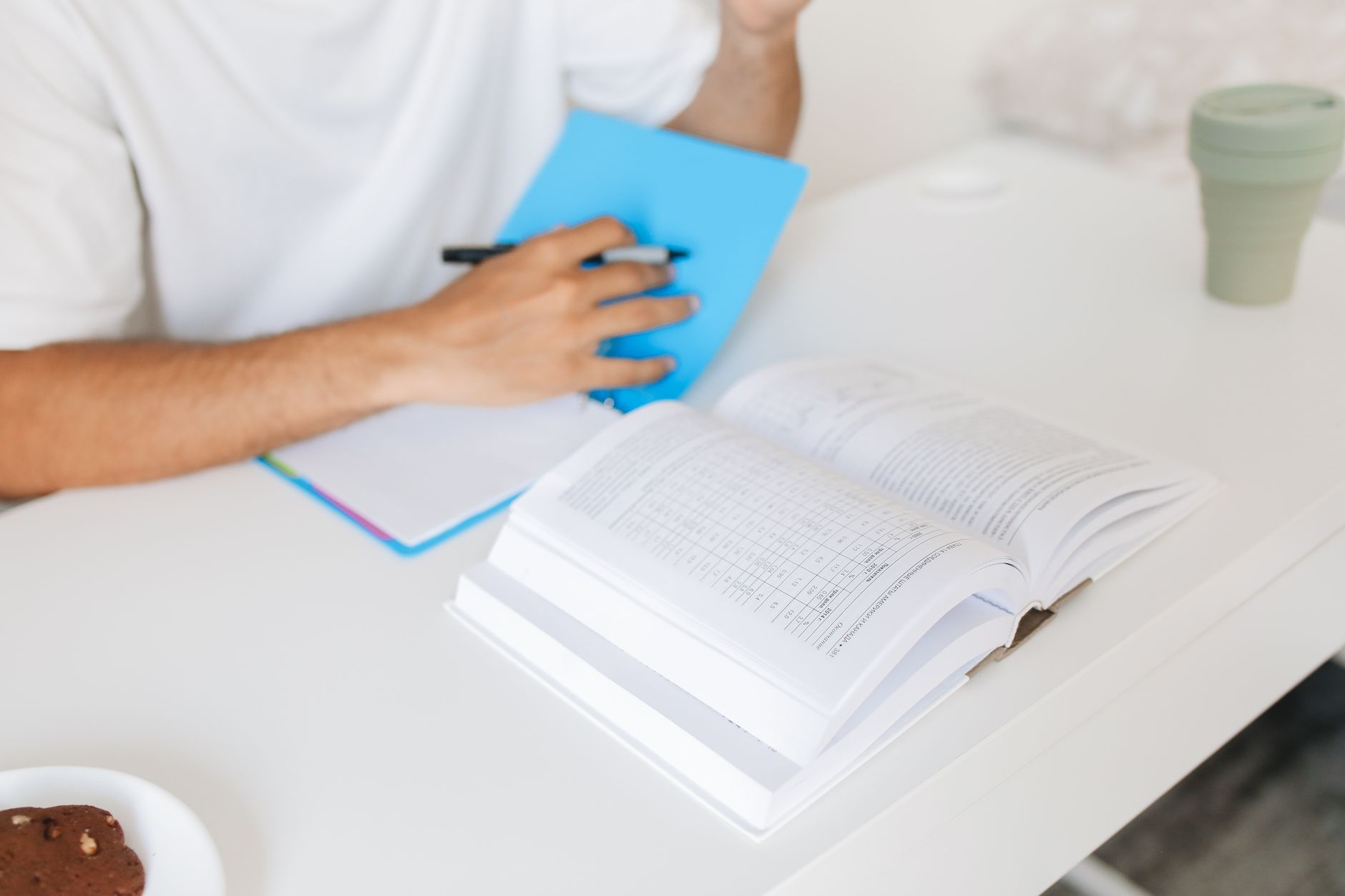 Persona tomando apuntes en una libreta junto a un libro de consulta abierto sobre la mesa