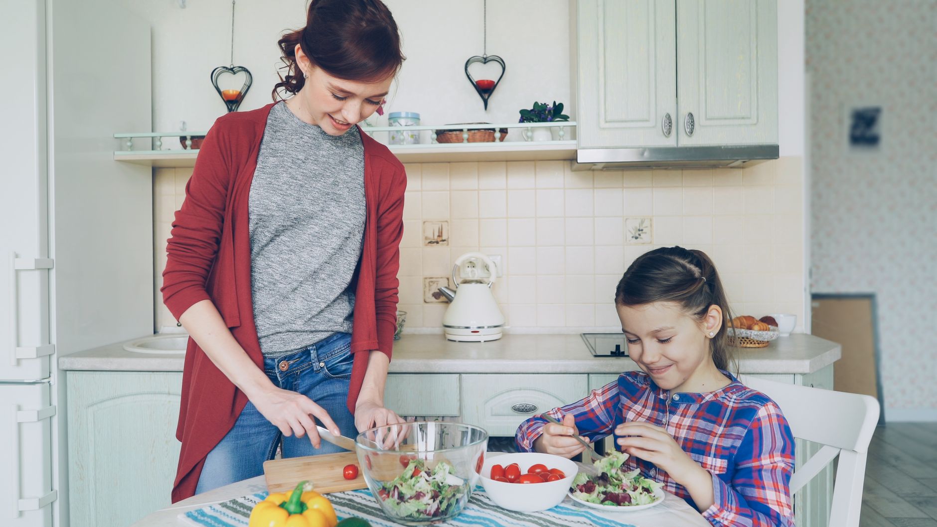 Madre e hija preparan una ensalada con tomates y pimentón en la mesa de la cocina