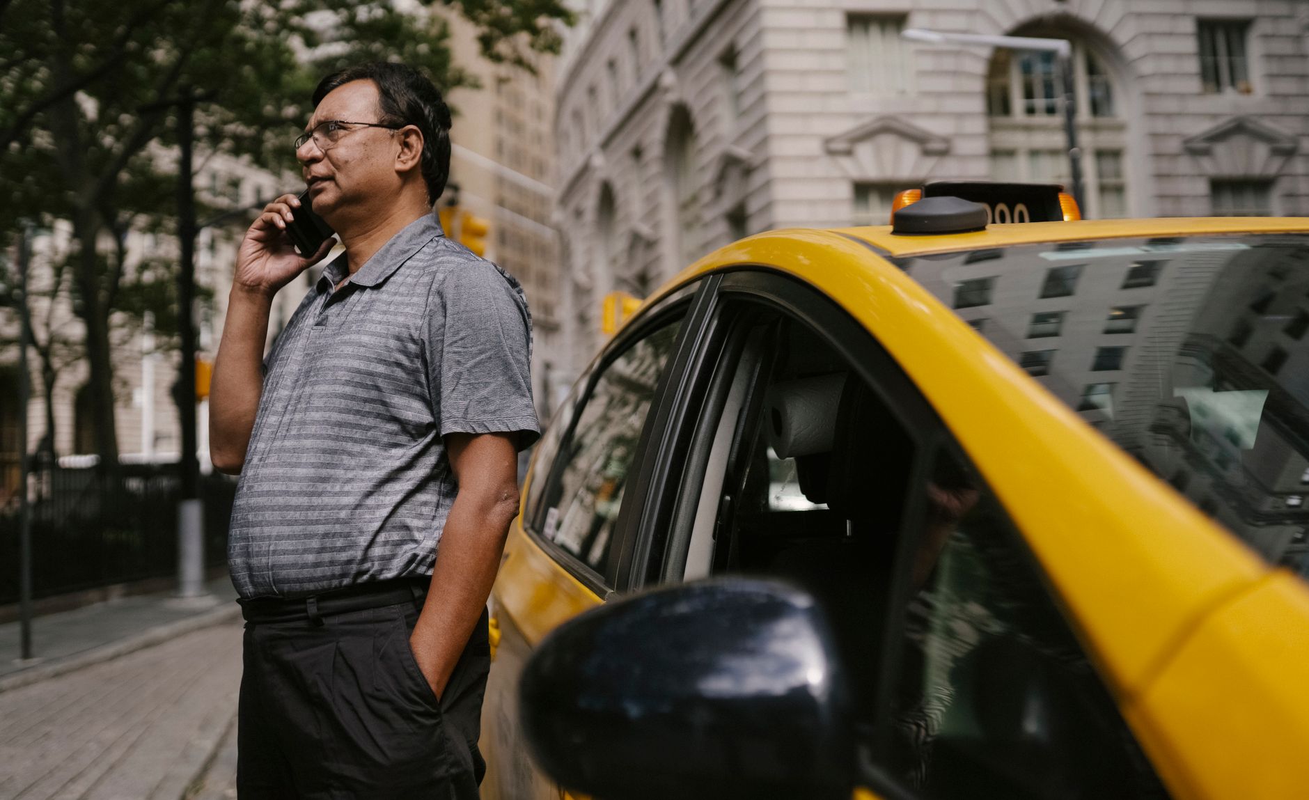 Un taxista habla por telefono en la acera, junto a su carro amarillo