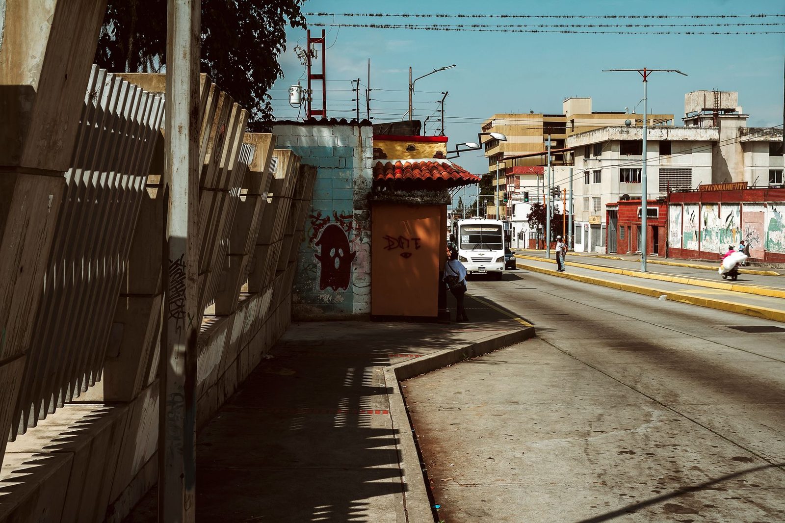 Avenida de una ciudad venezolana con una camionetica de pasajeros, comercios y gente esperando el transporte