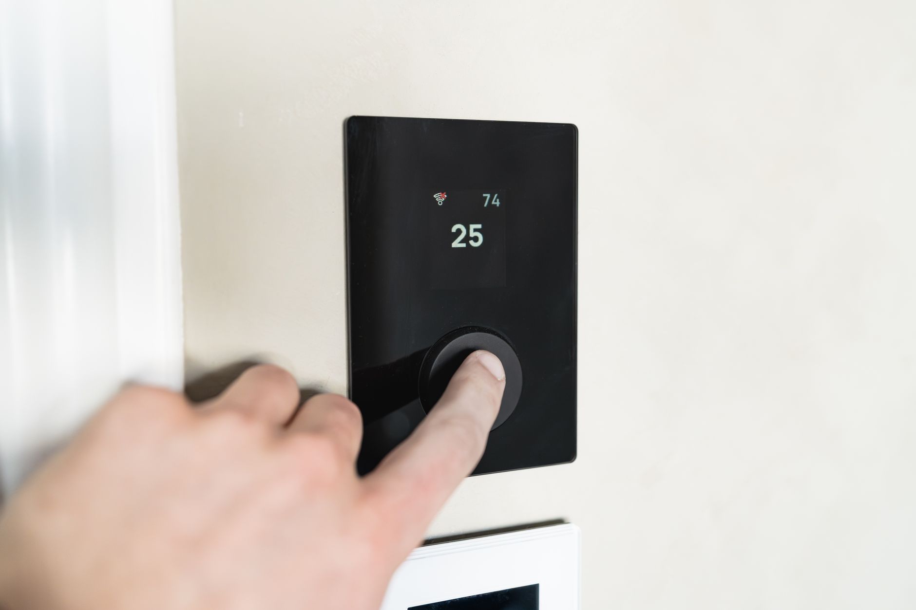 Un dedo pulsa el mando de un termostato de pared que marca 25 grados y muestra el icono de conexión wifi