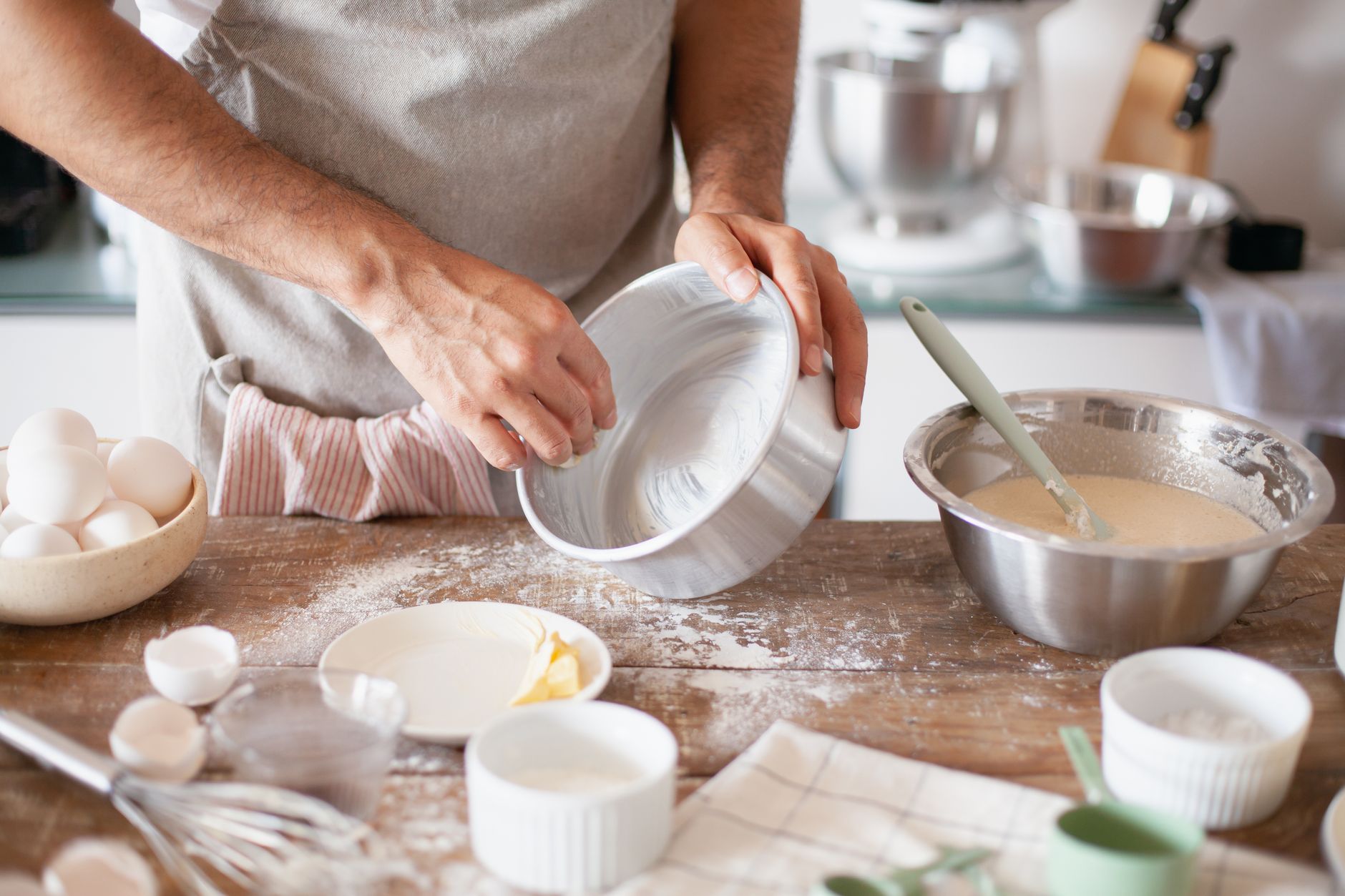 Manos engrasando con mantequilla un molde redondo de aluminio sobre una mesa de cocina