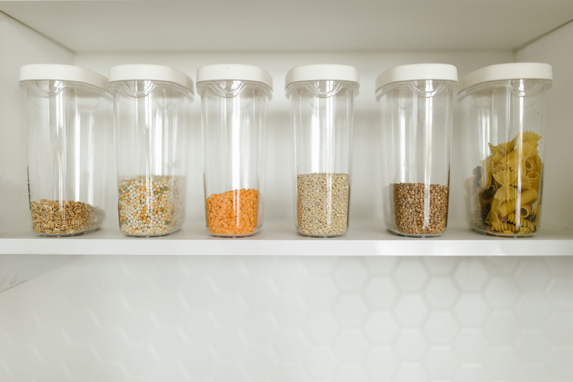 Envases transparentes del mismo tamano alineados en una repisa con el contenido a la vista