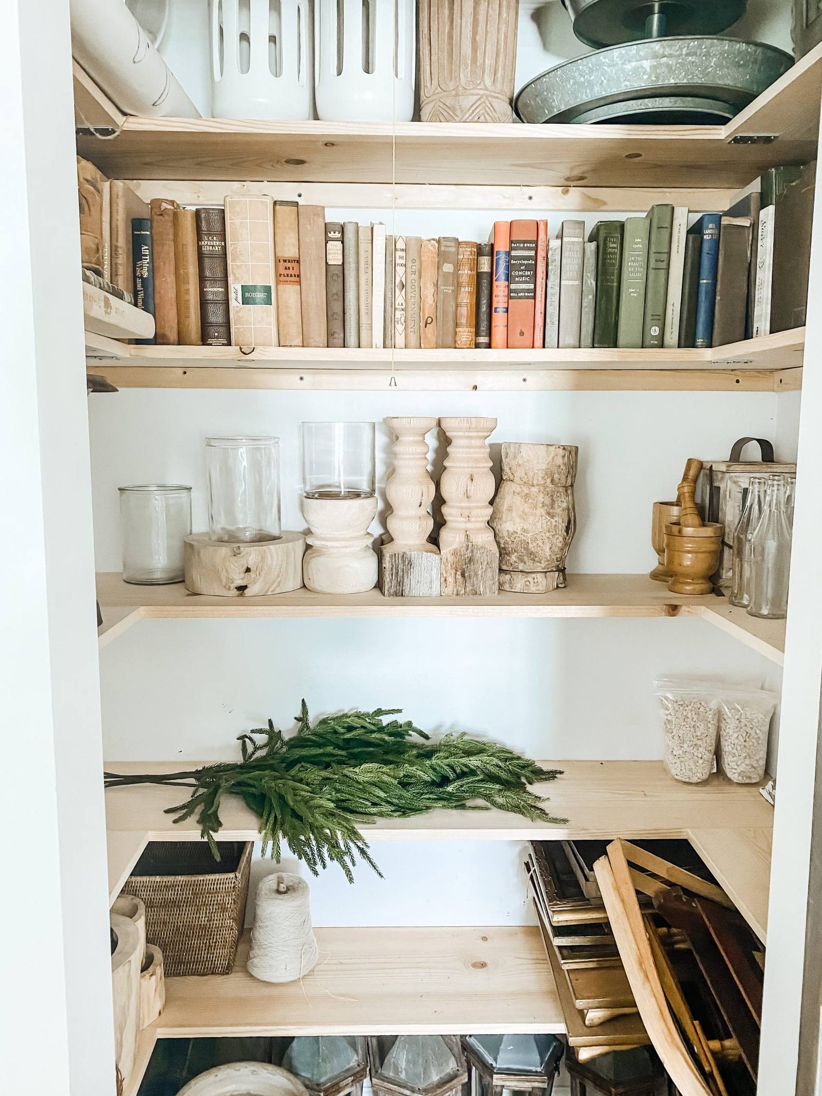 Estanterías de madera de una despensa con libros antiguos, velas, morteros, un manojo de ramas verdes y frascos de vidrio