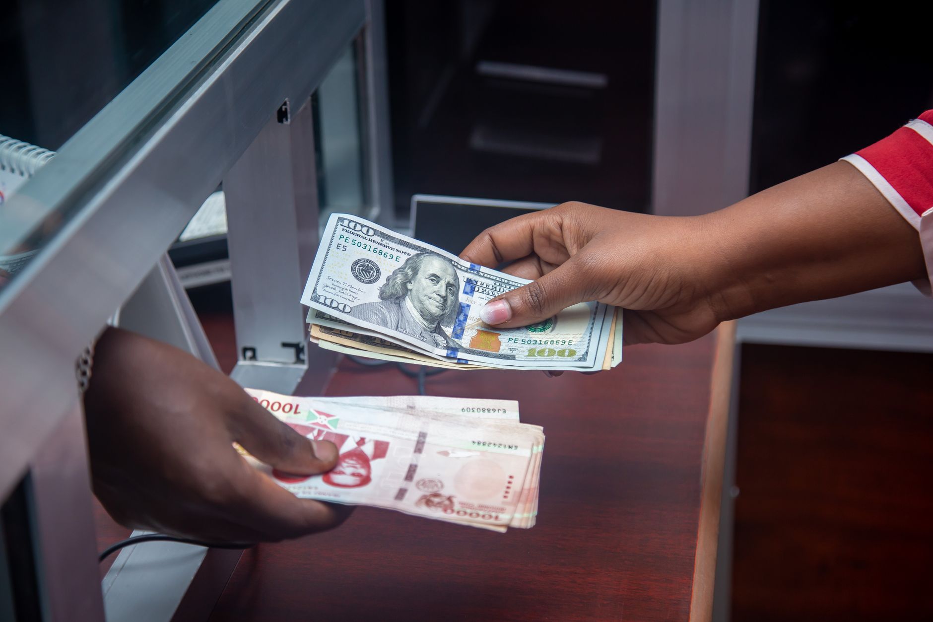 Manos intercambiando billetes de dolar por moneda local en la ventanilla de una casa de cambio