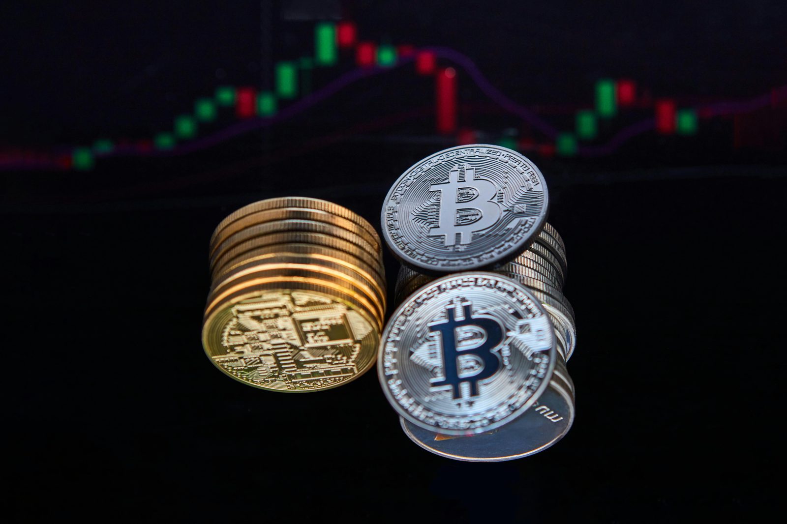 Monedas físicas de Bitcoin, unas doradas y otras plateadas, apiladas sobre una superficie oscura con un gráfico de fondo