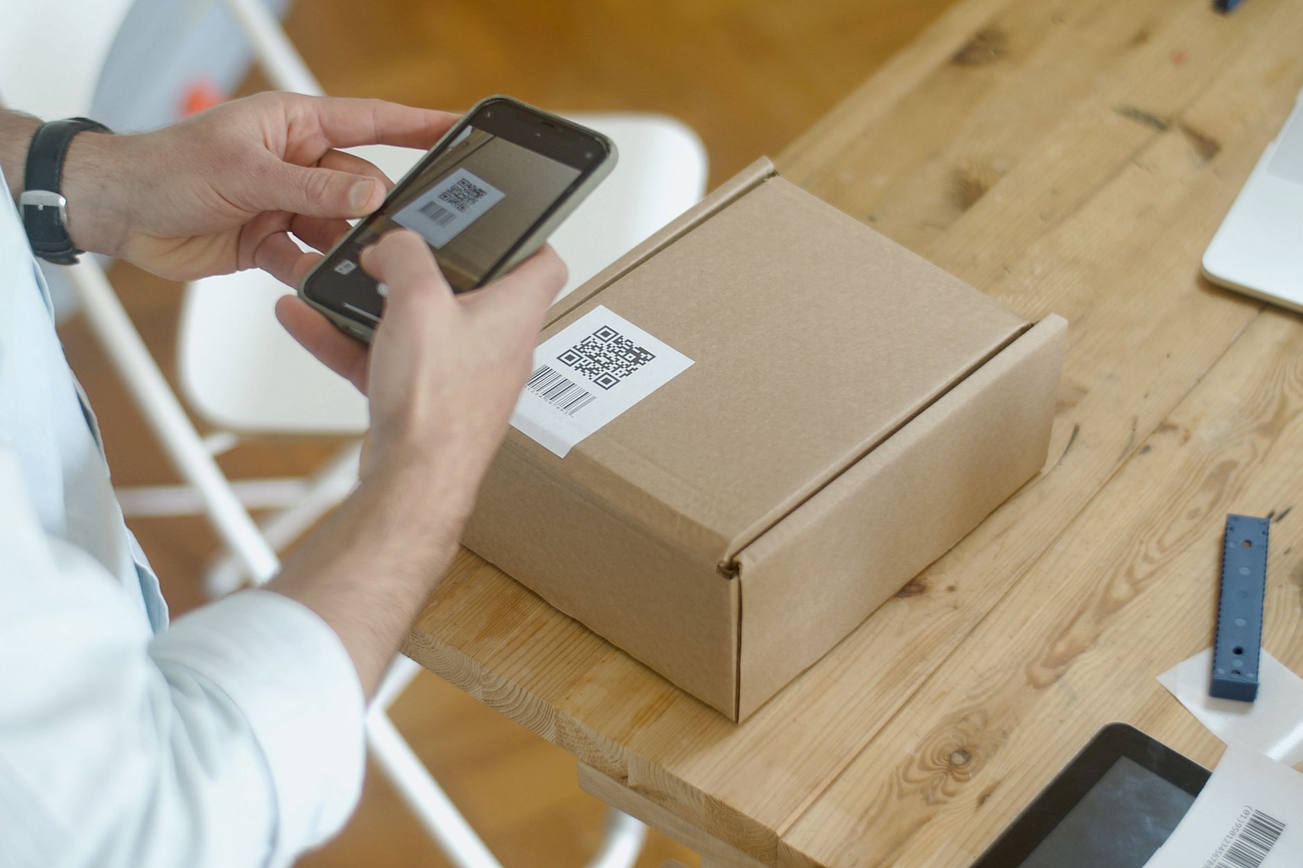 Una persona escanea con el móvil el código QR pegado en una caja de cartón sobre una mesa de madera