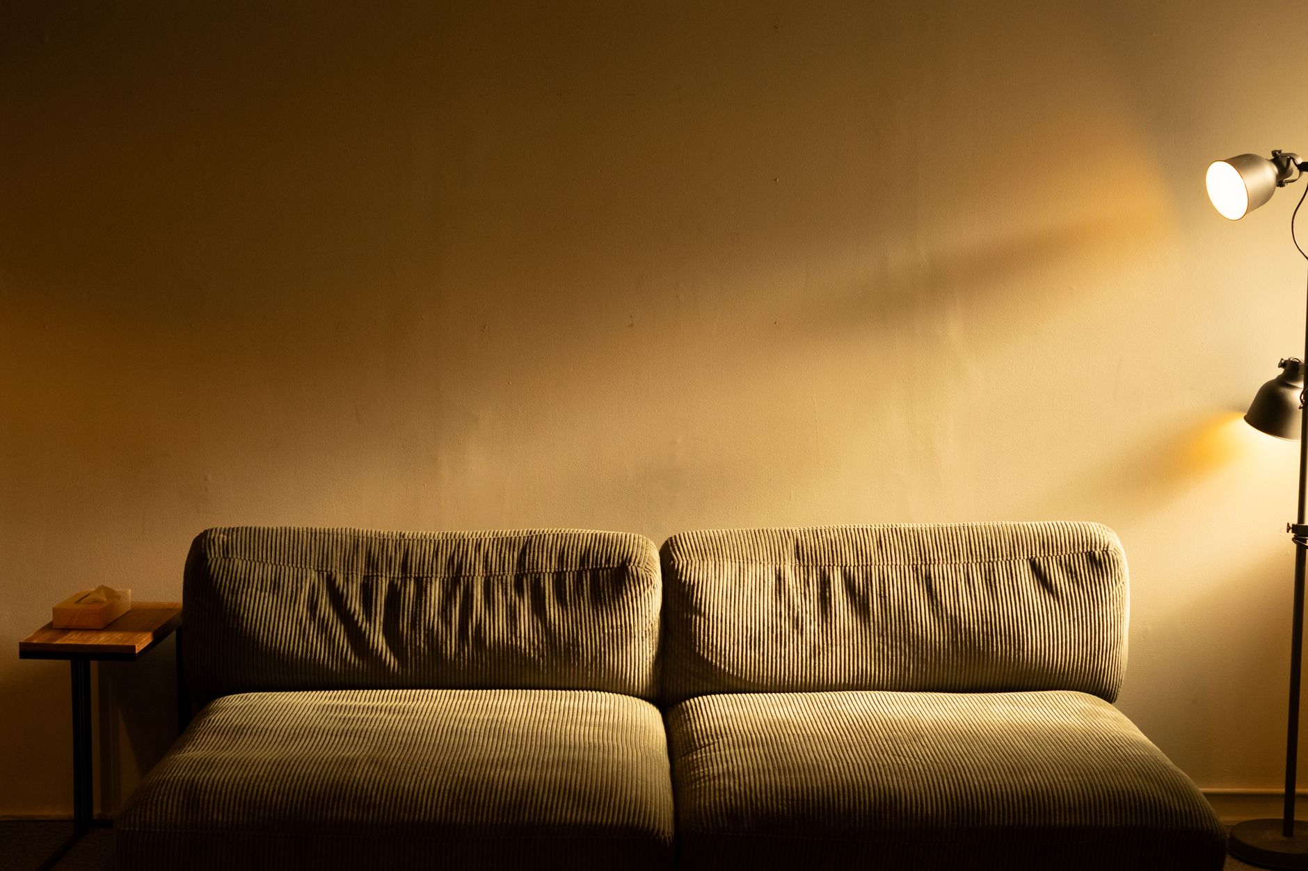 Sofá de pana iluminado por una lámpara de pie de luz cálida contra una pared lisa