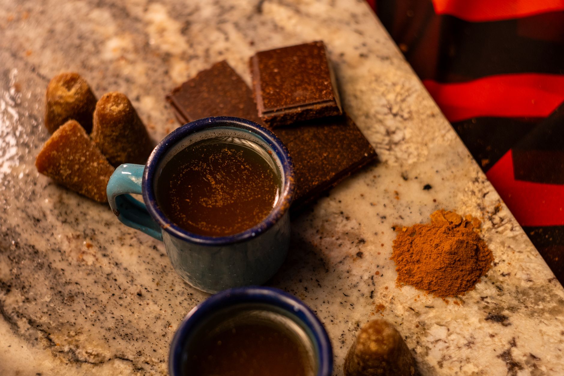 Conos de piloncillo marrón junto a una taza de café, cuadros de chocolate y canela molida sobre una encimera de granito