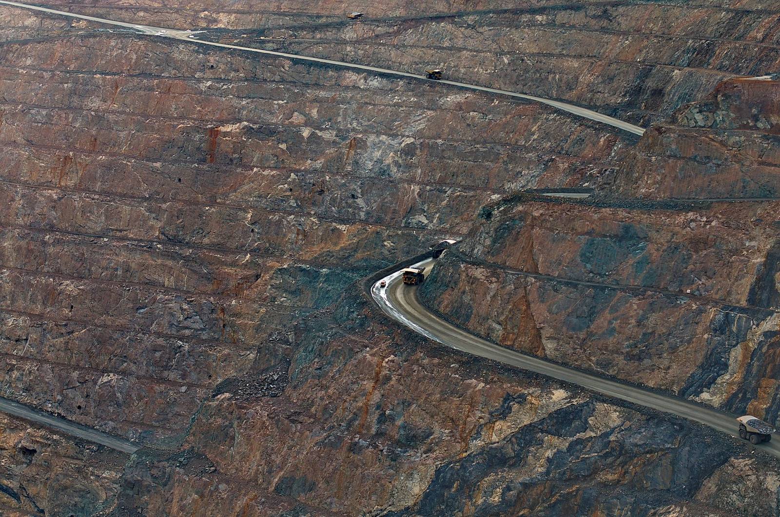 Vista aérea de una mina a cielo abierto con camiones subiendo por las rampas entre roca mineralizada