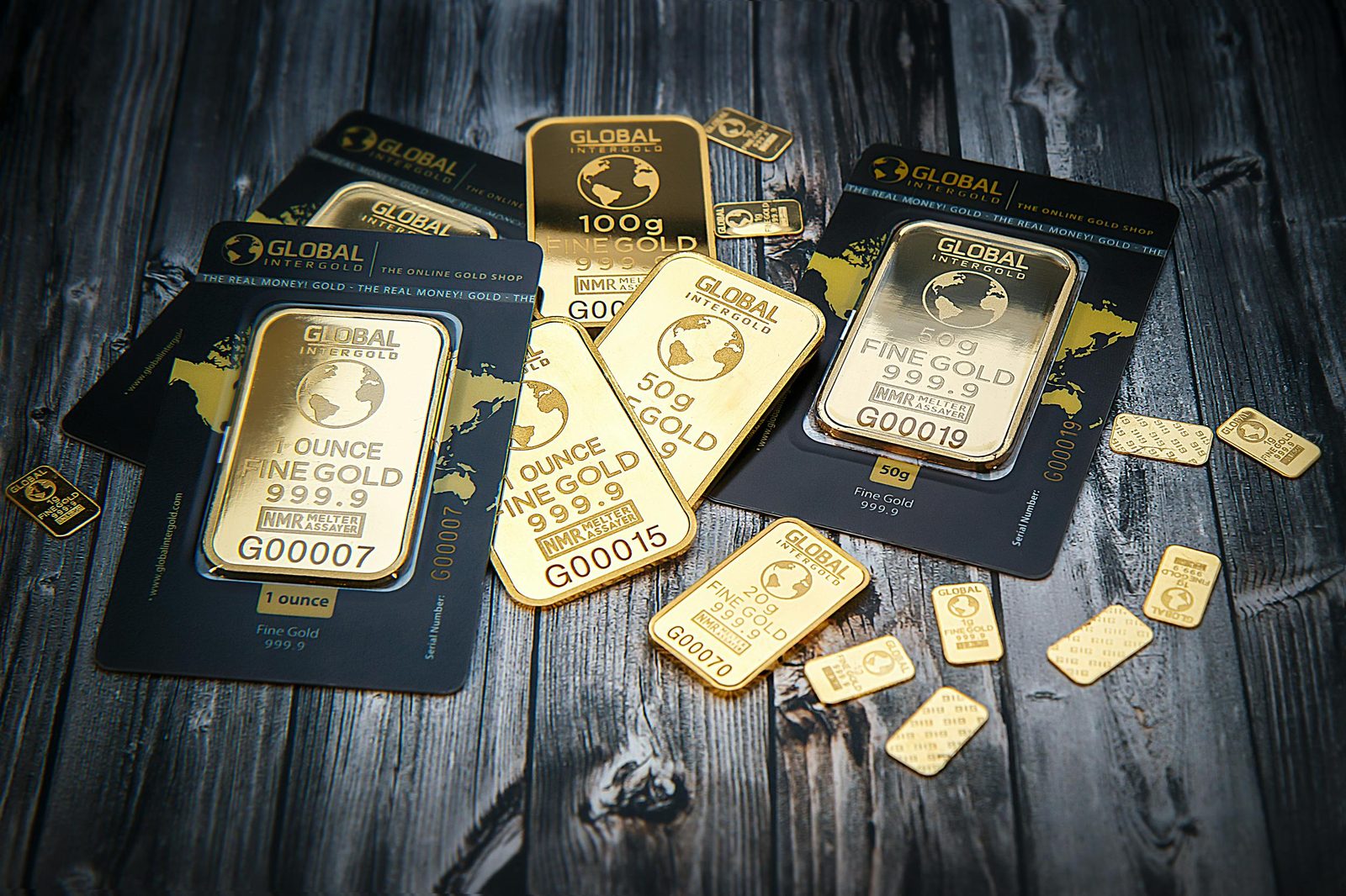 Varias barras de oro de 1 onza, 50g y 100g con empaques negros de Global Intergold sobre una superficie oscura