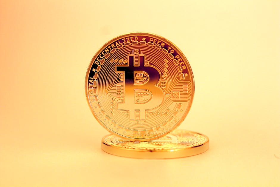 Moneda dorada de Bitcoin erguida sobre otra moneda metálica en un fondo beige claro