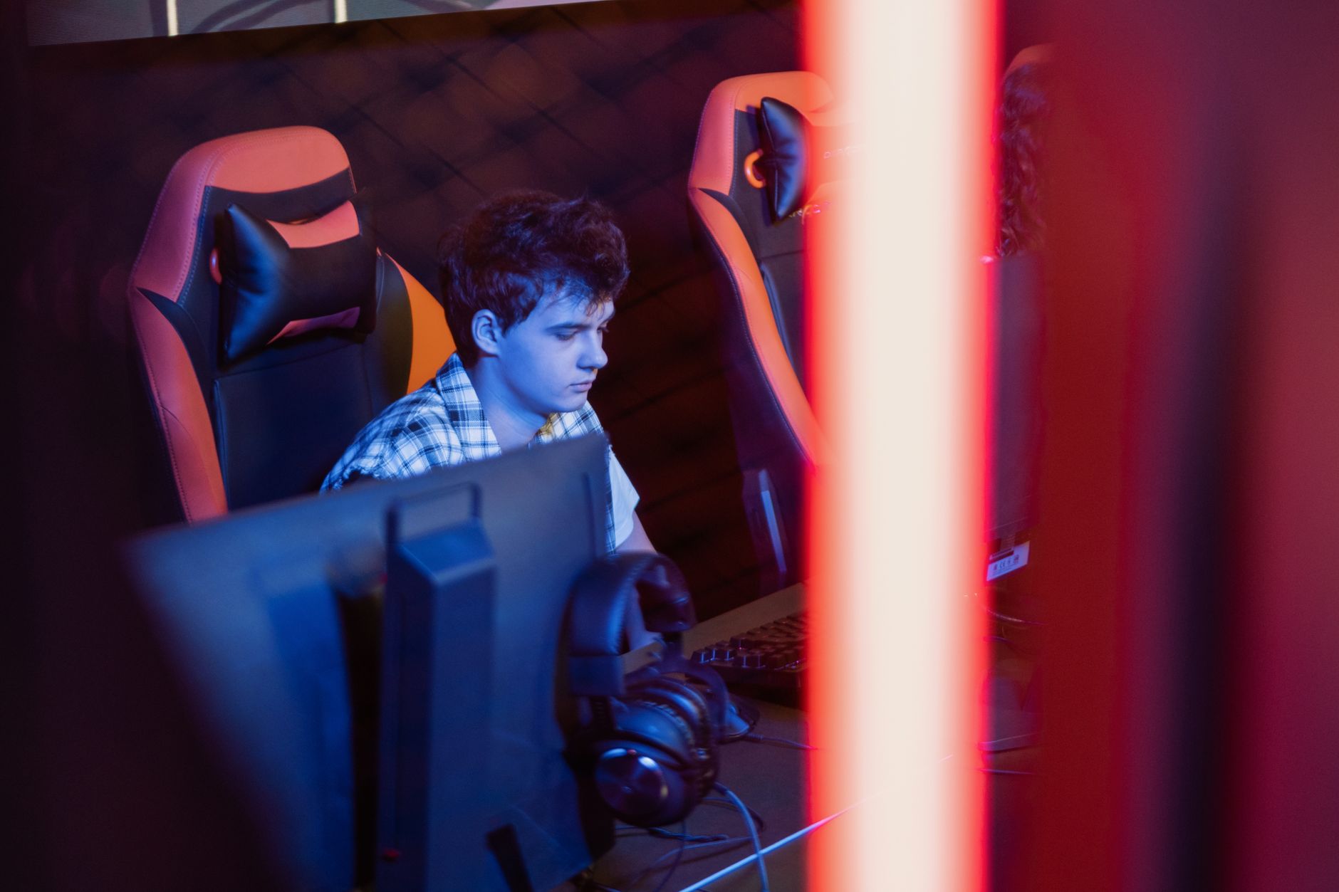 Joven jugando en una computadora de escritorio en un local de videojuegos iluminado con luces de neón
