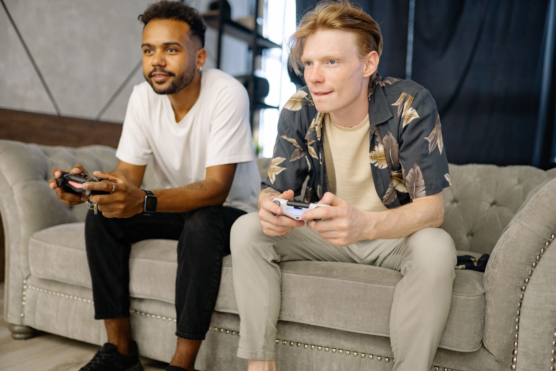 Dos amigos sentados en el sofá de una sala jugando videojuegos con los mandos en la mano