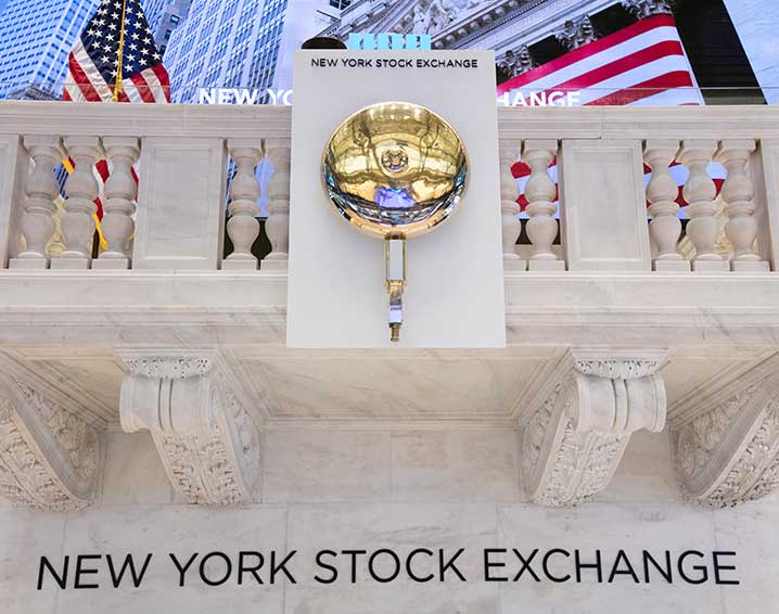 Fachada de mármol de la Bolsa de Nueva York con la campana de trading dorada y pantallas con banderas estadounidenses