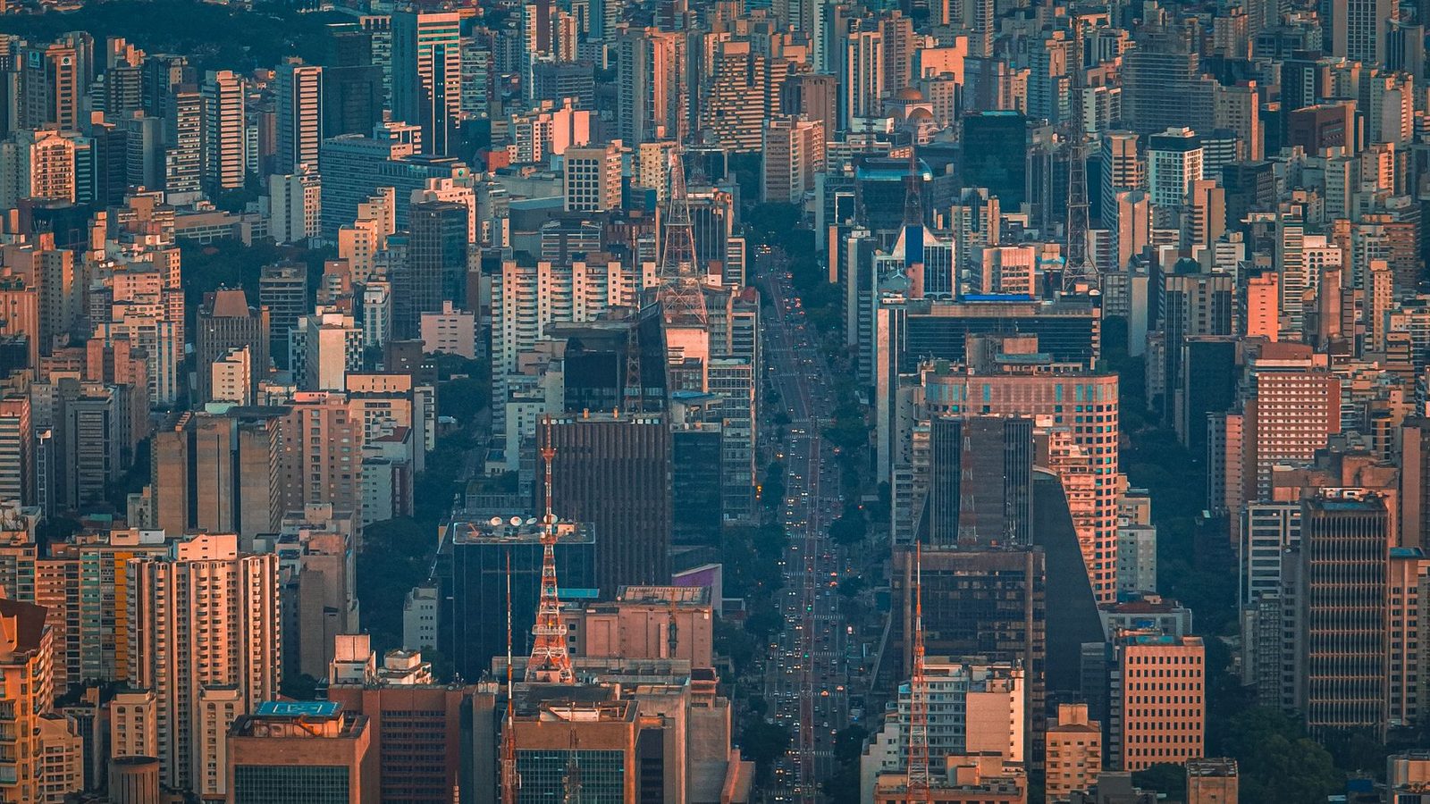 Vista aerea del centro de Sao Paulo al anochecer, con una avenida cargada de trafico entre torres de oficinas y una grua de obra