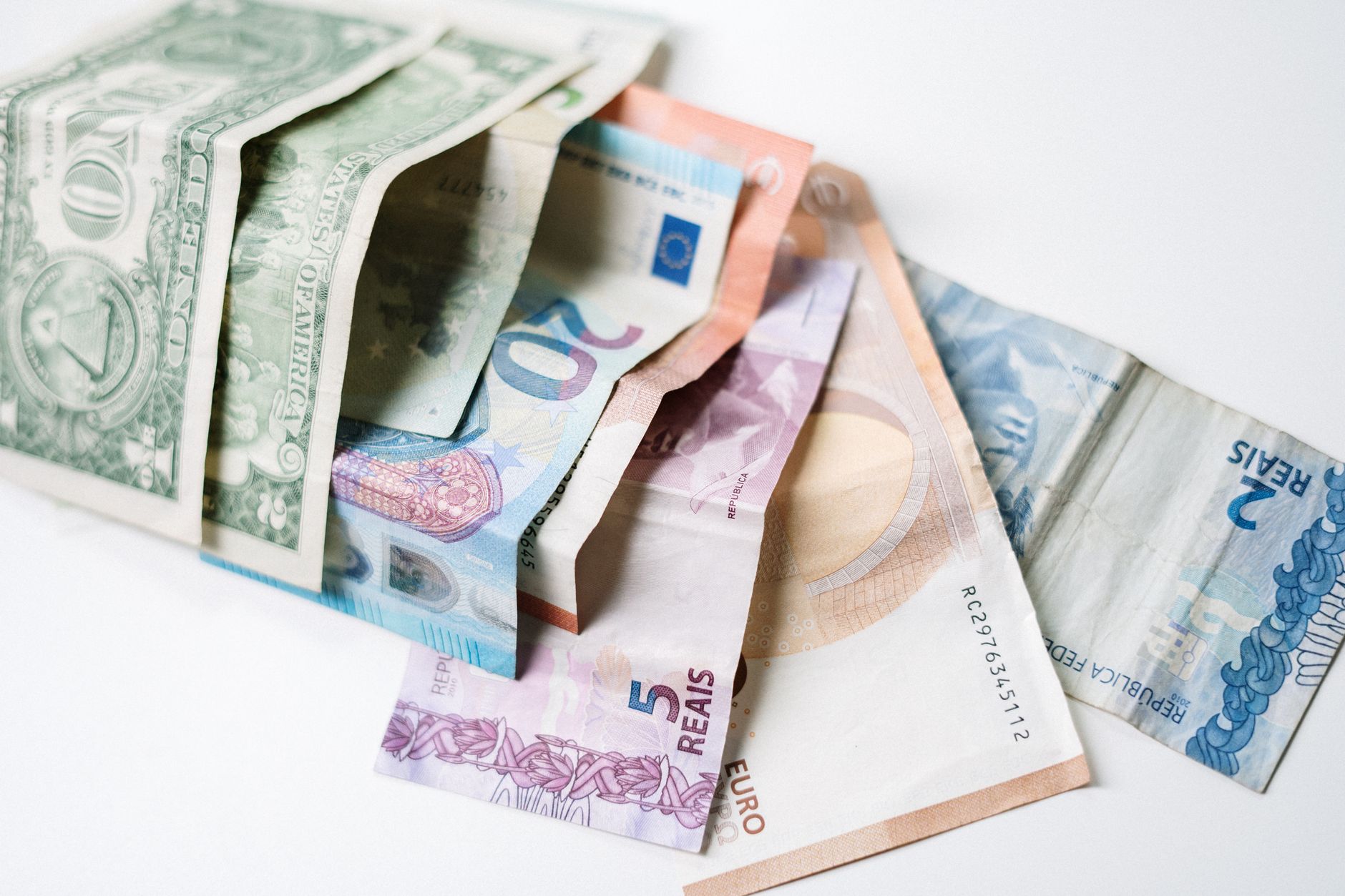 Billetes de dólar, euro y real brasileño extendidos en abanico sobre una superficie blanca