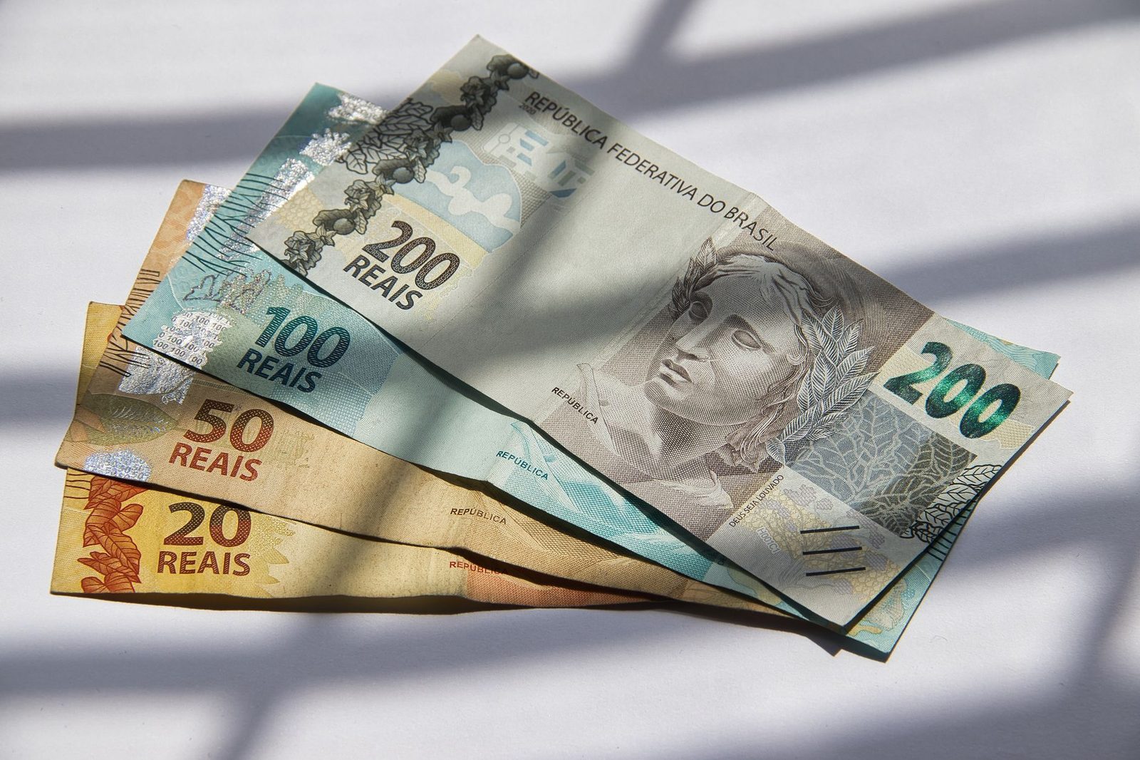 Billetes de veinte, cincuenta, cien y doscientos reales brasileños desplegados en abanico bajo la luz de una ventana