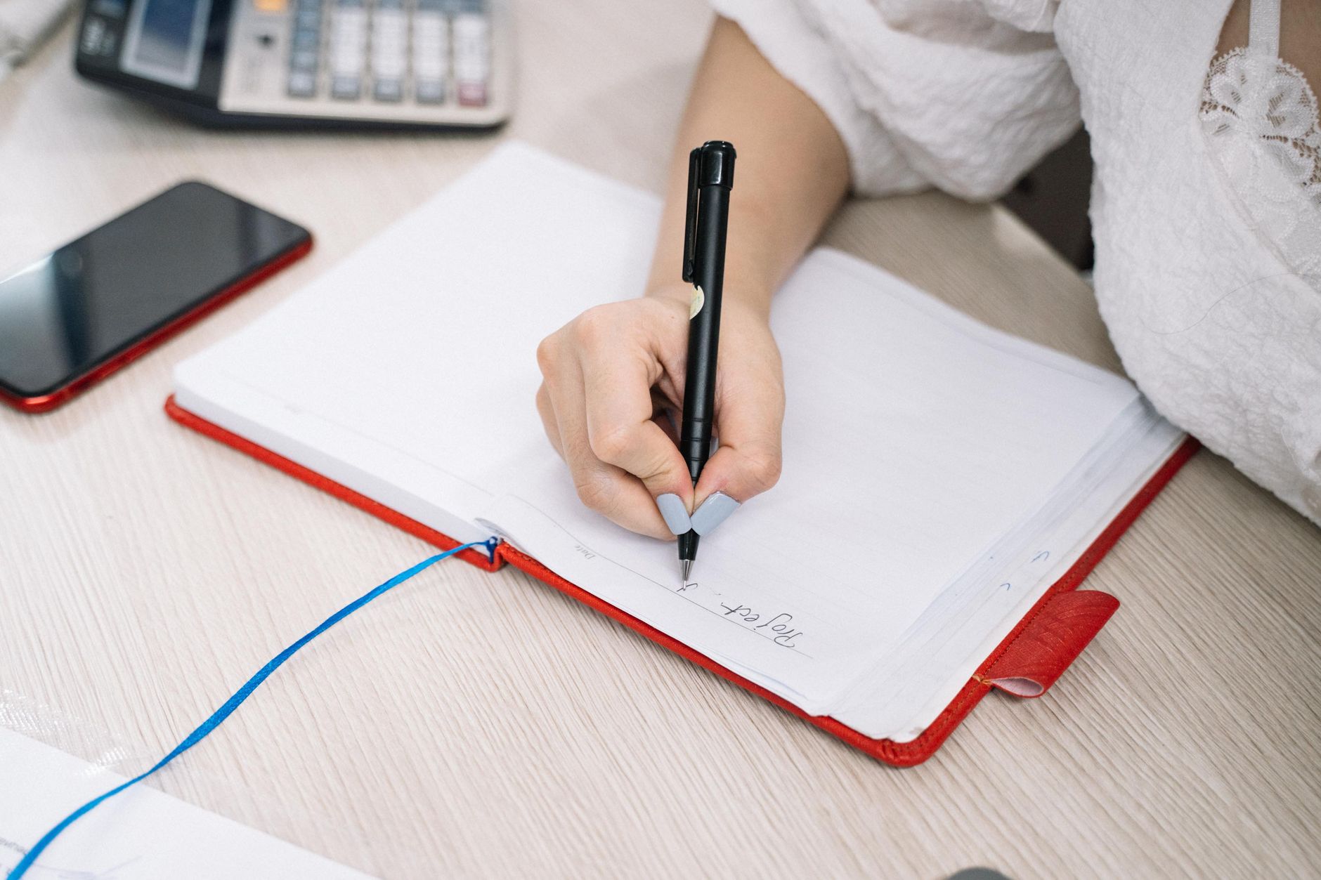 Mano escribiendo un plan de operaciones en una libreta, con una calculadora y un teléfono sobre el escritorio