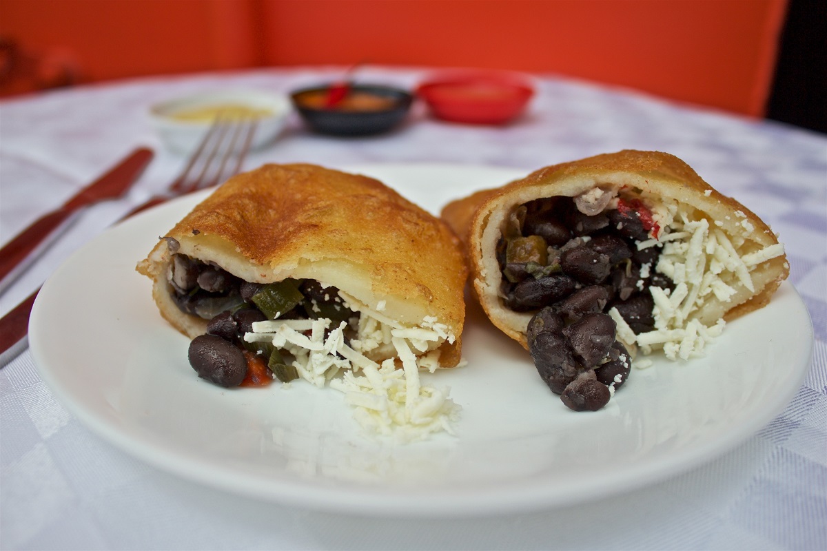 Dos empanadas fritas abiertas con relleno de frijoles negros y queso rallado, servidas en un plato blanco