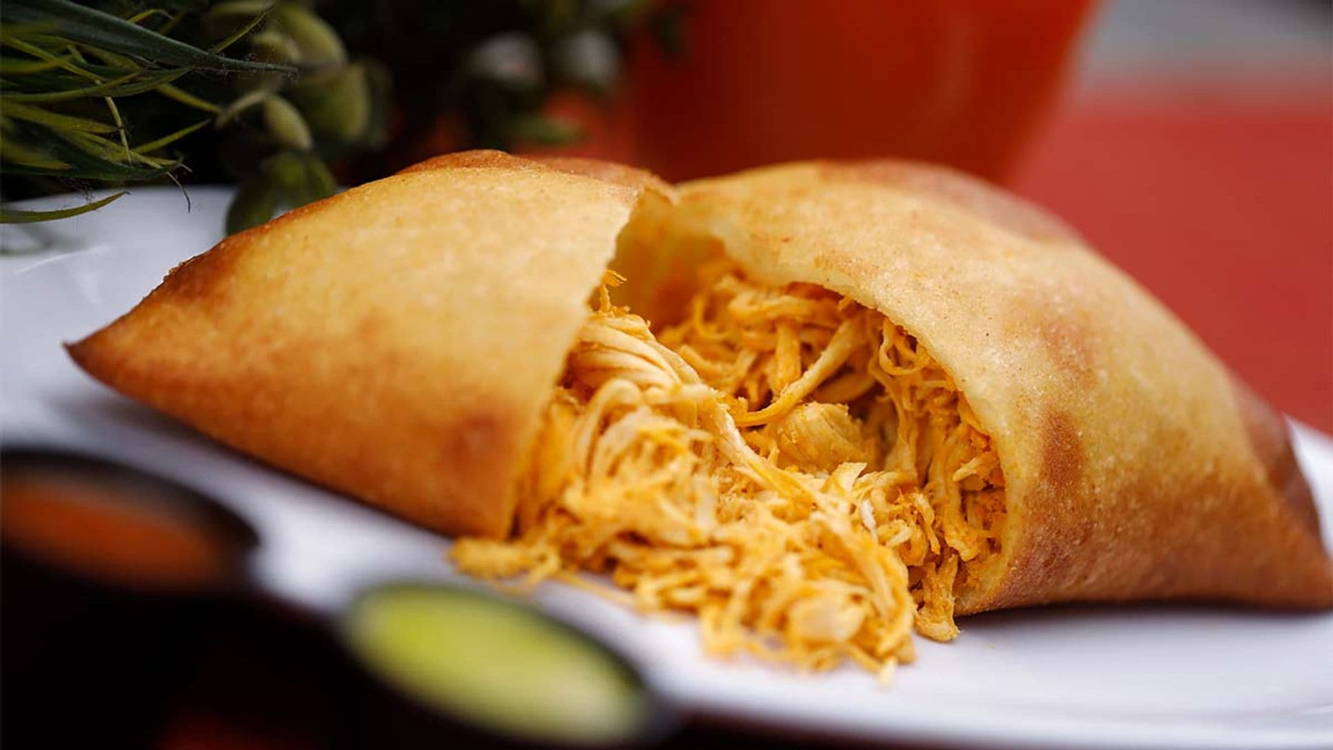 Empanada frita de maíz partida por la mitad, mostrando abundante relleno de pollo desmenuzado sobre un plato blanco