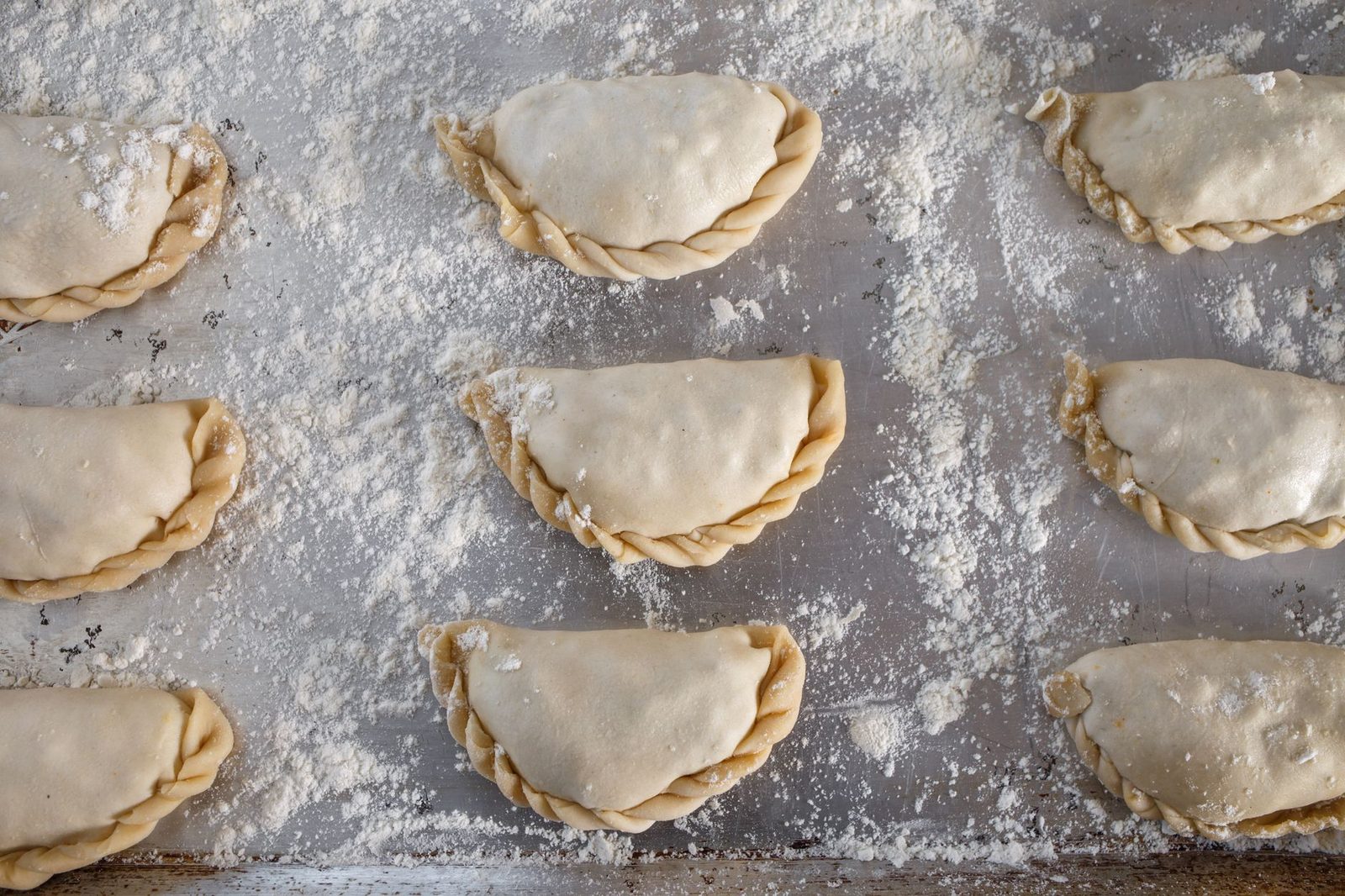 Empanadas crudas separadas sobre una bandeja enharinada, listas para congelar