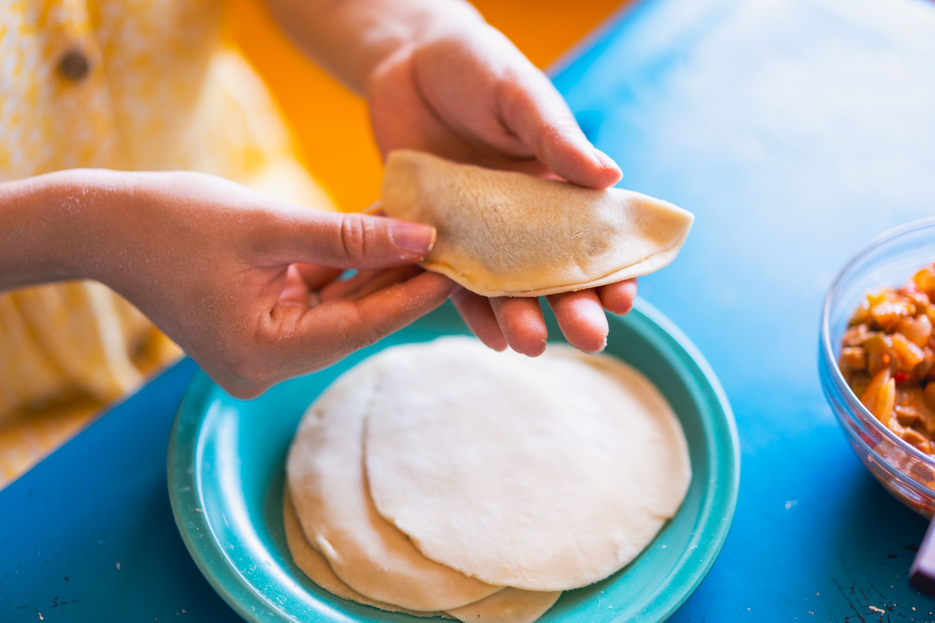 Discos de masa apilados en un plato y una empanada ya cerrada en forma de media luna sostenida en la mano