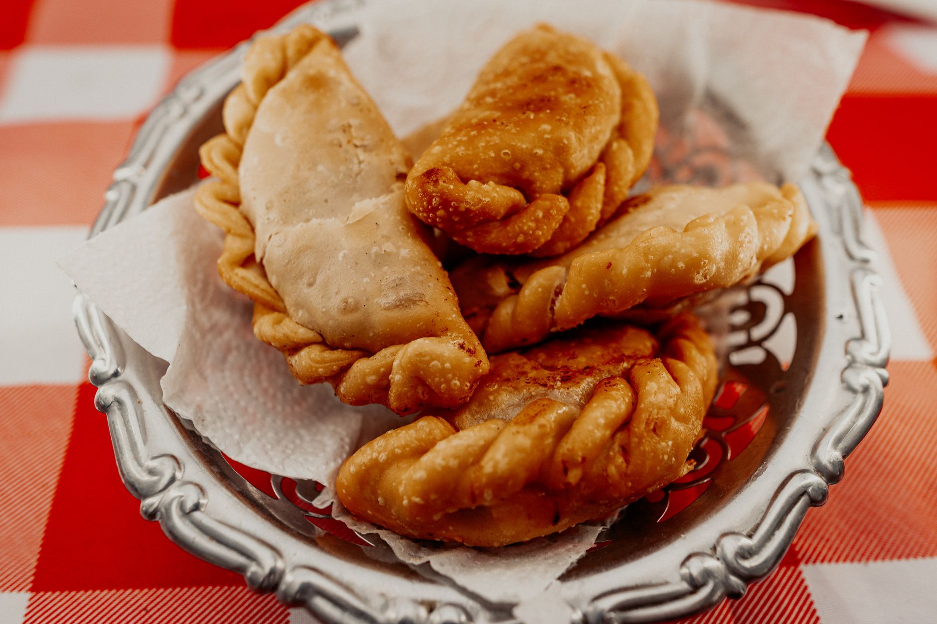 Empanadas recién fritas servidas sobre papel en una bandeja, encima de un mantel de cuadros rojos