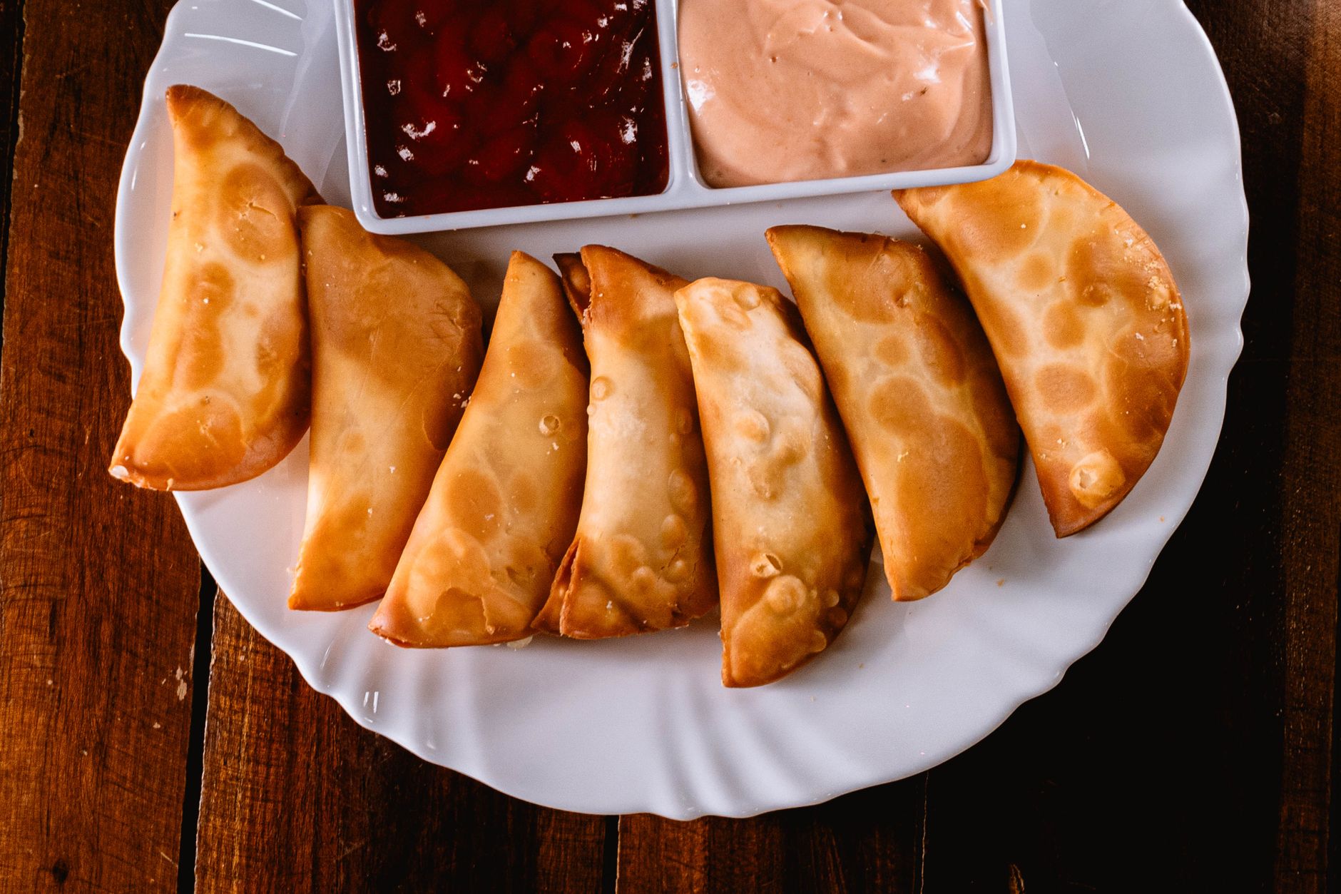 Empanadas fritas doradas en abanico sobre un plato blanco junto a dos salsas para mojar