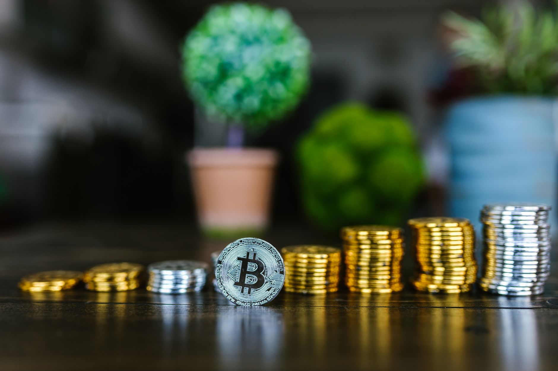 Ficha de bitcoin apoyada junto a columnas de monedas apiladas de distinta altura sobre una mesa de madera