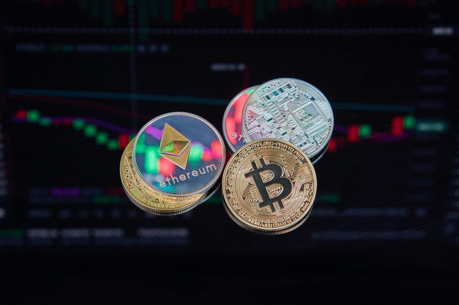 Monedas físicas de Bitcoin, Ethereum y XRP sobre una superficie oscura y reflectante con un gráfico financiero