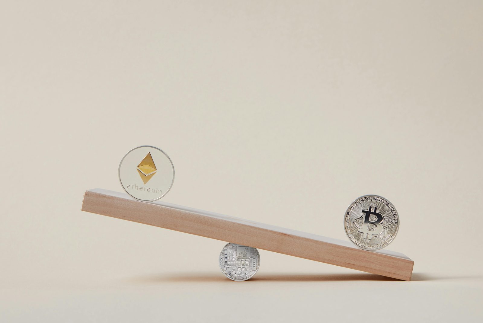 Monedas de Ethereum y Bitcoin colocadas en una balanza de madera con otra moneda bajo el punto de apoyo