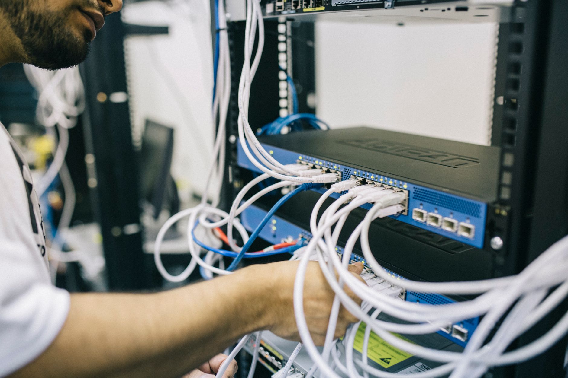 Un técnico conecta cables de red en un armario de servidores lleno de latiguillos blancos y azules