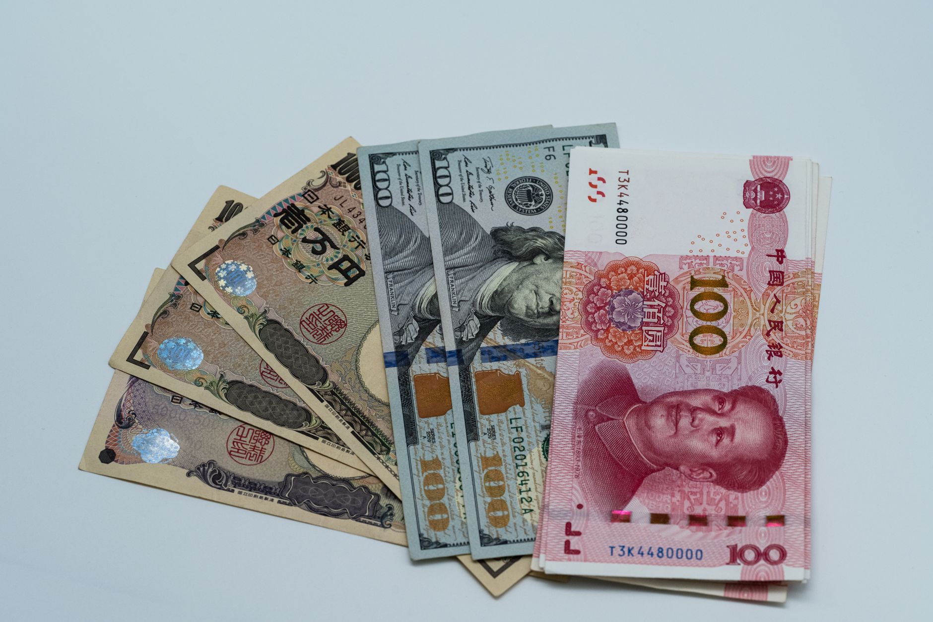 Billetes de yen, dolar y yuan extendidos uno junto a otro sobre una superficie clara