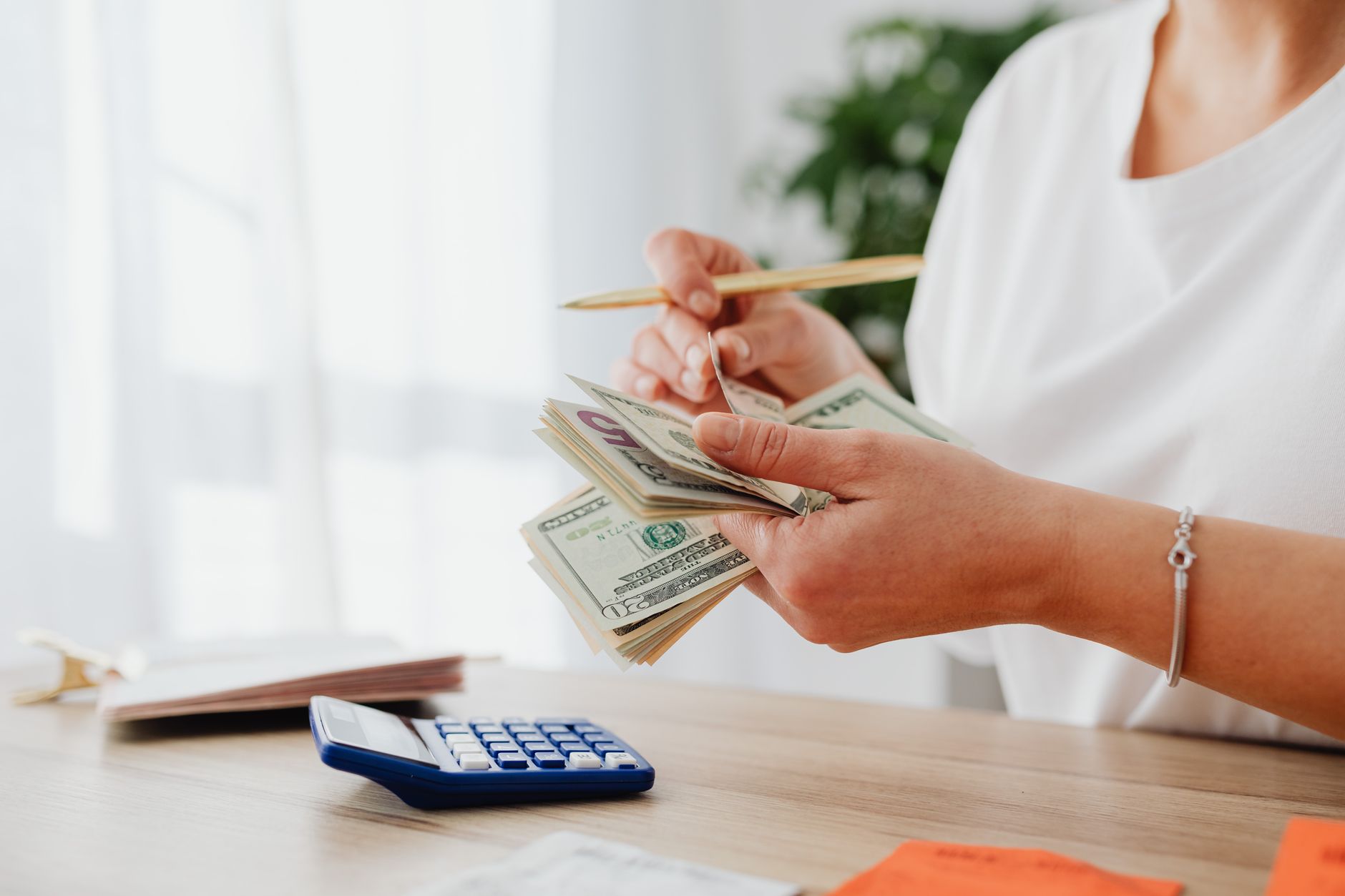 Manos contando billetes de dólar junto a una calculadora sobre la mesa de casa