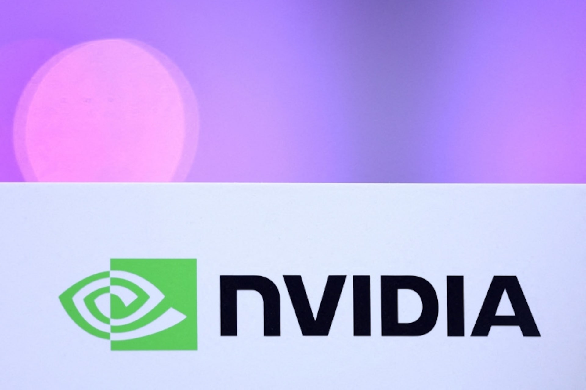 Logotipo verde y negro de NVIDIA sobre un fondo blanco, con un efecto bokeh púrpura difuminado en la parte superior