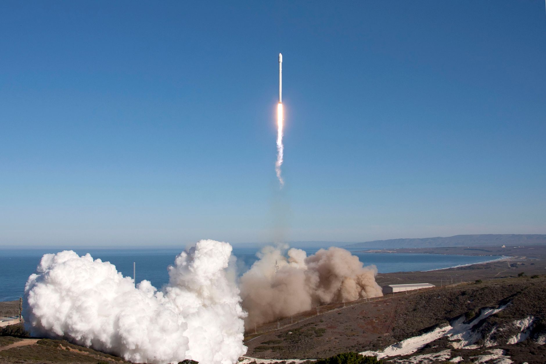 Cohete despegando desde una plataforma junto al océano entre columnas de humo blanco