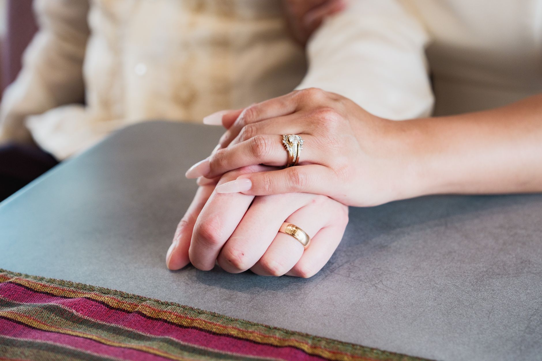 Manos de una pareja casada entrelazadas sobre una mesa, con los anillos a la vista