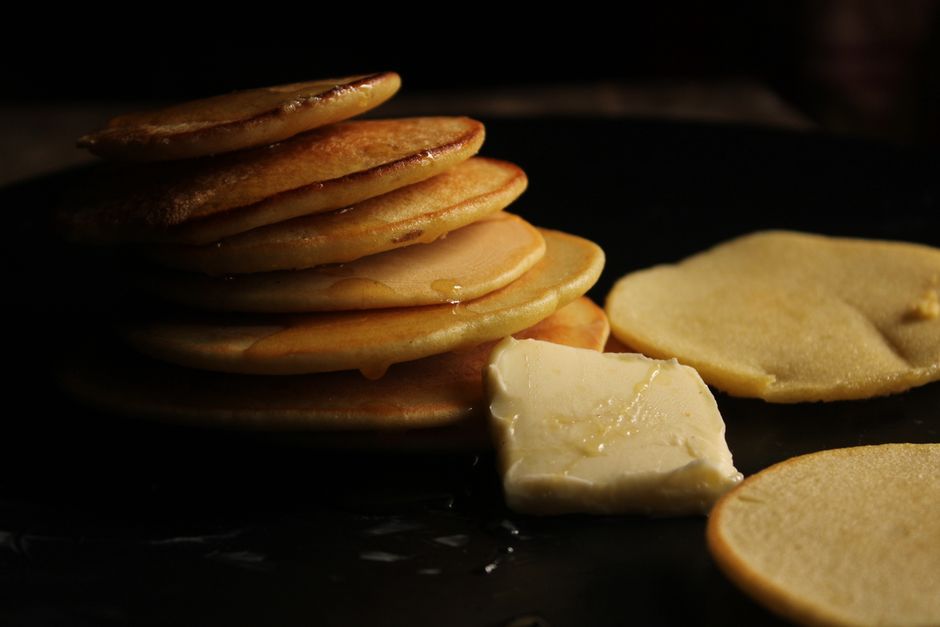 Pila de tortitas doradas sobre una plancha oscura con una pieza de mantequilla al lado