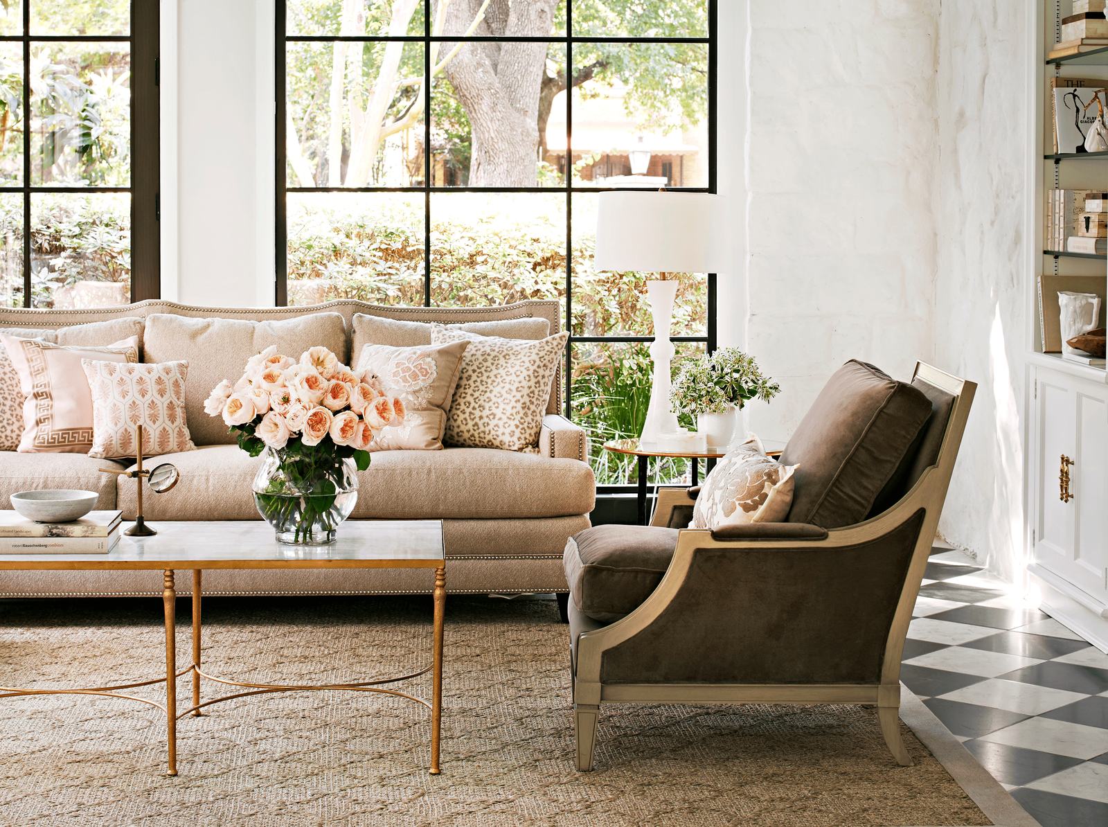 Sala de estar con sofá beige, cojines estampados, mesa de centro con flores y una silla marrón.